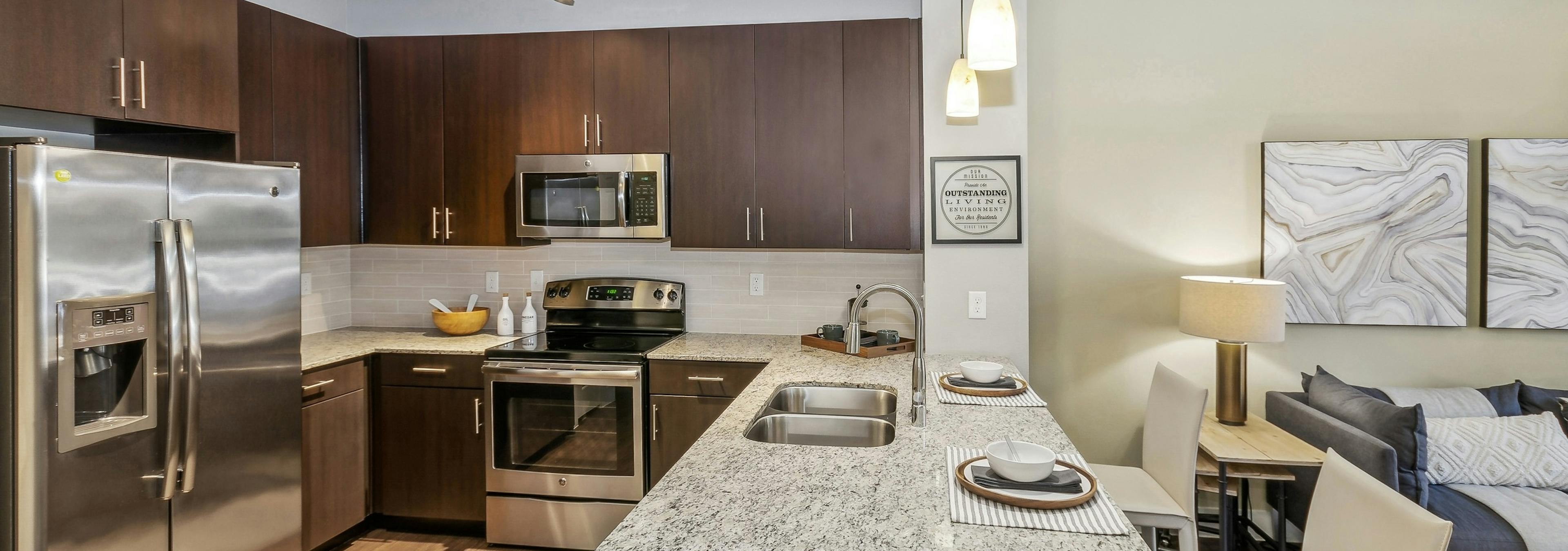 AMLI West Plano apartment kitchen with granite countertops and espresso wood cabinets and stainless appliances adjacent to the living room 