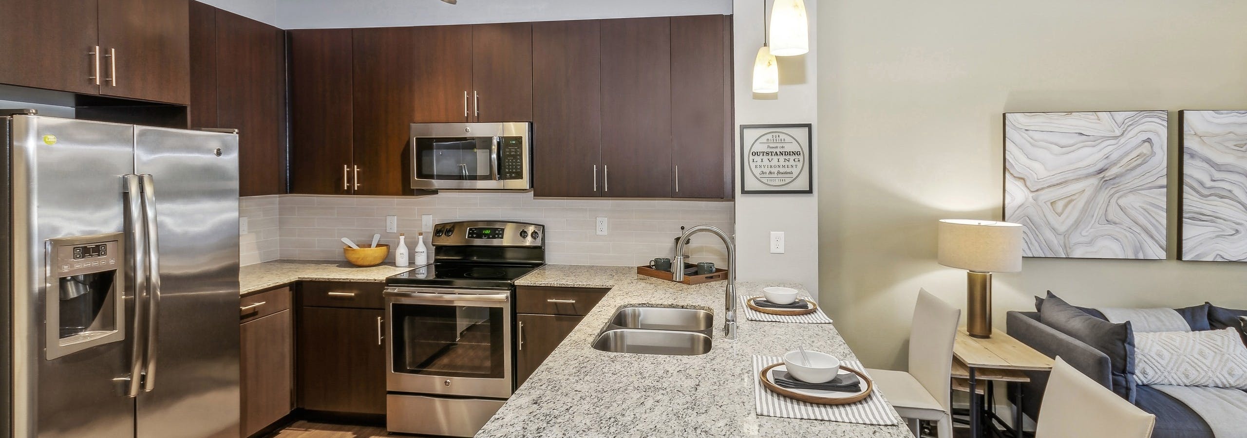 AMLI West Plano apartment kitchen with granite countertops and espresso wood cabinets and stainless appliances adjacent to the living room