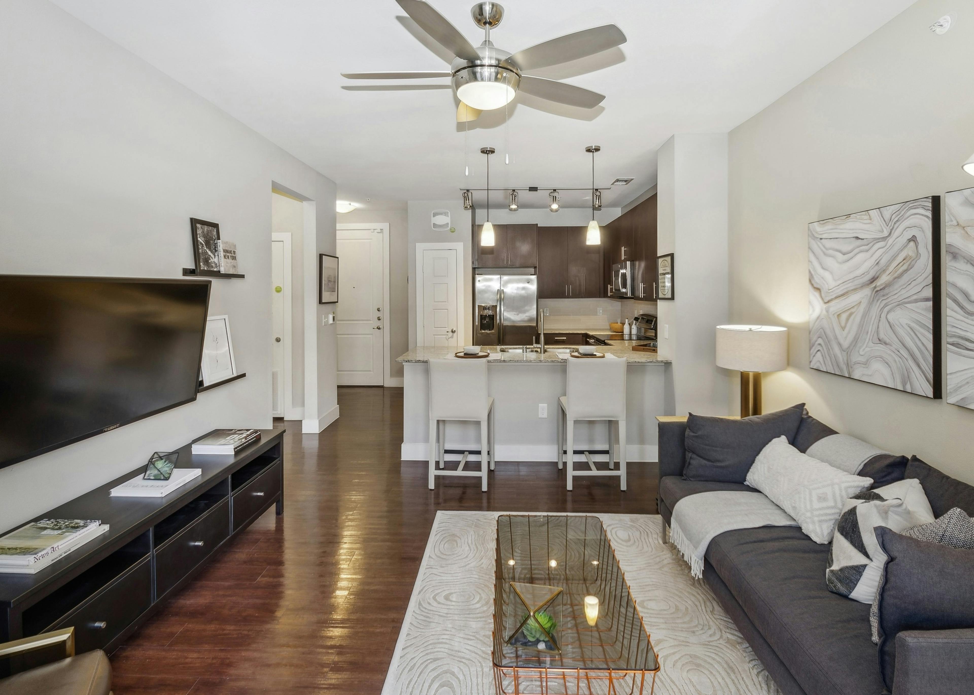 AMLI West Plano living room with gray couch facing TV on hardwood floors looking toward an open kitchen with breakfast bar 