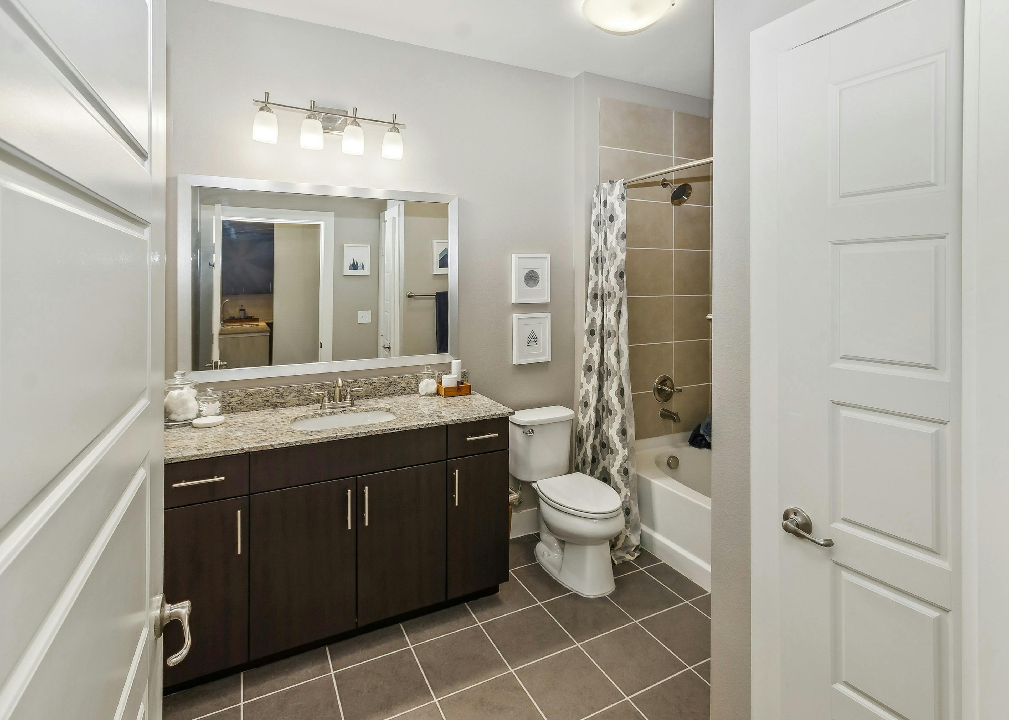 AMLI West Plano bathroom featuring a dark wood vanity with a granite countertop below a large mirror adjacent to a bathtub with shower