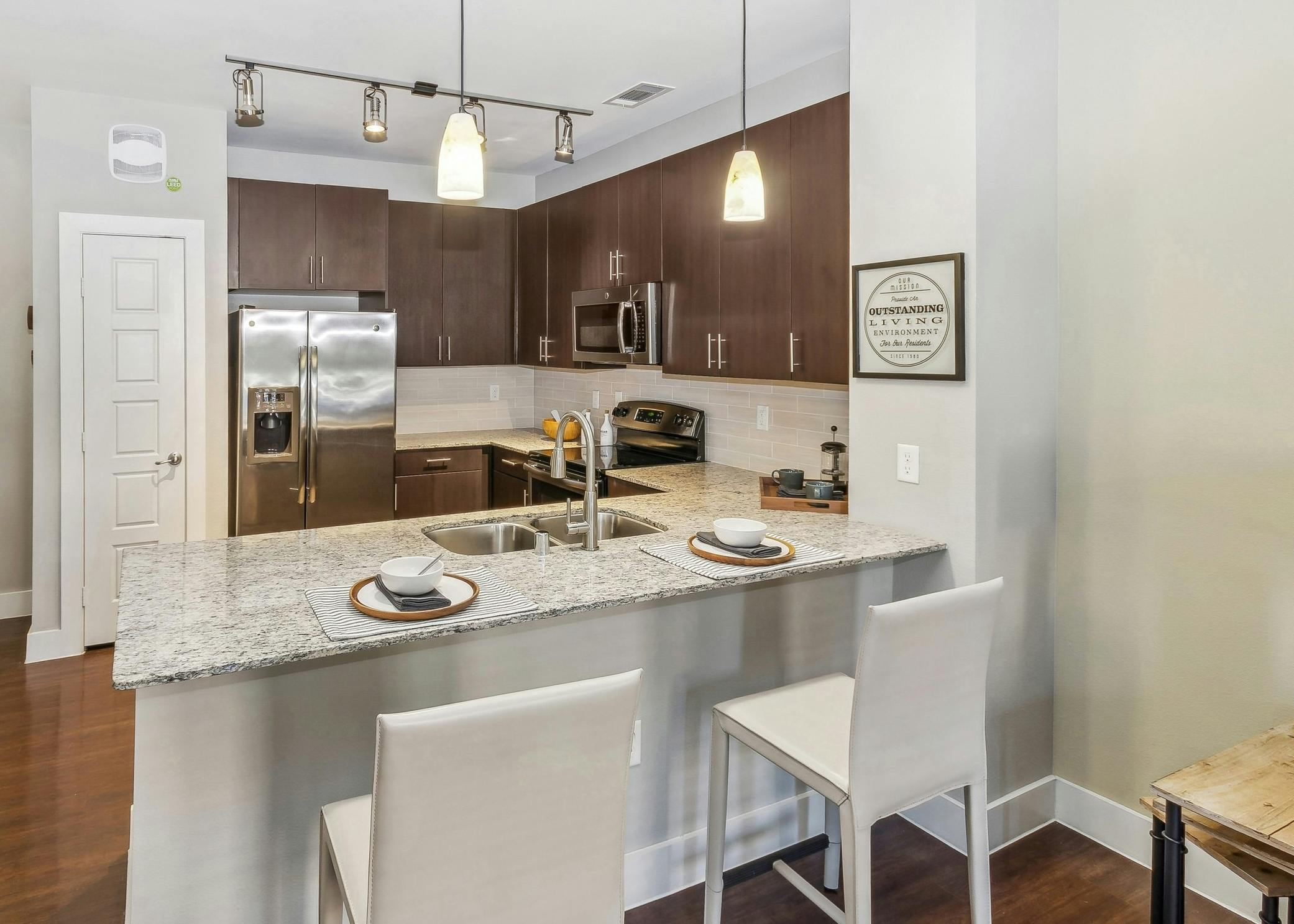 Kitchen with stainless appliances and dark wood cabinets and granite countertops at AMLI West Plano with two bar stools at the breakfast bar