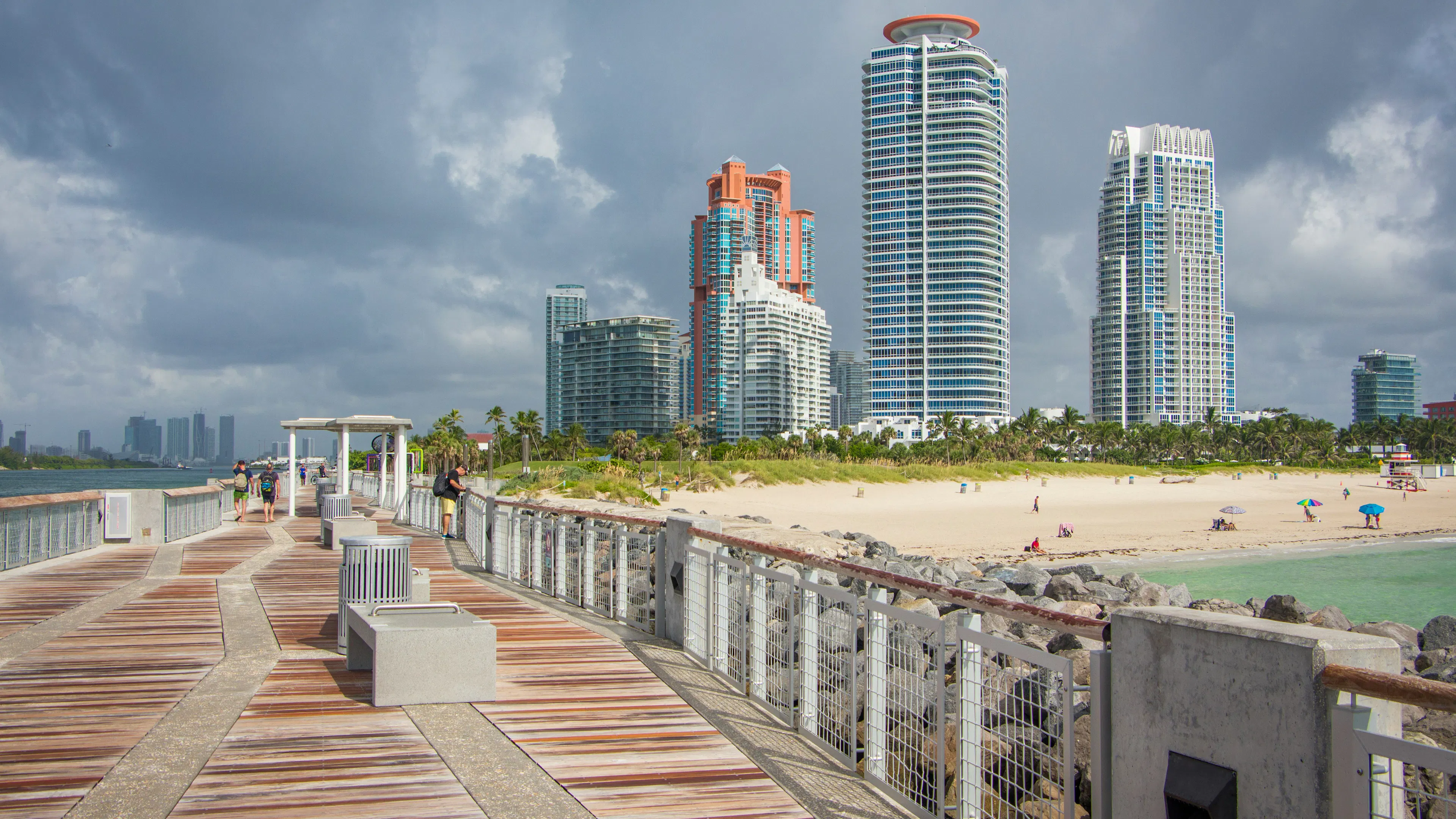 A wide wooden boardwalk alongside a scenic Florida beach with tall buildings in the background