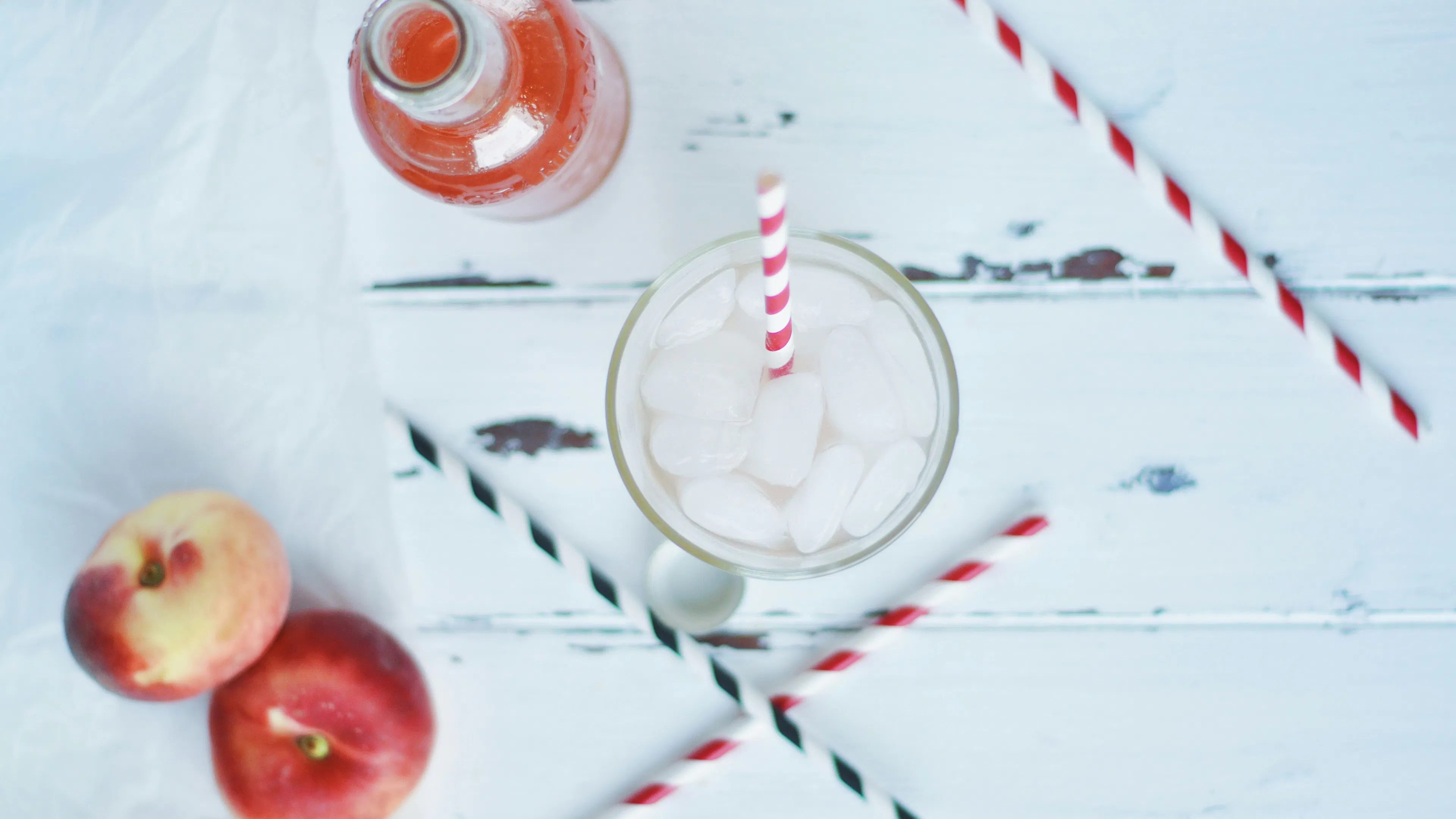 A glass filles with ice and peach iced tea viewed from above with peaches and peach juice placed around the glass