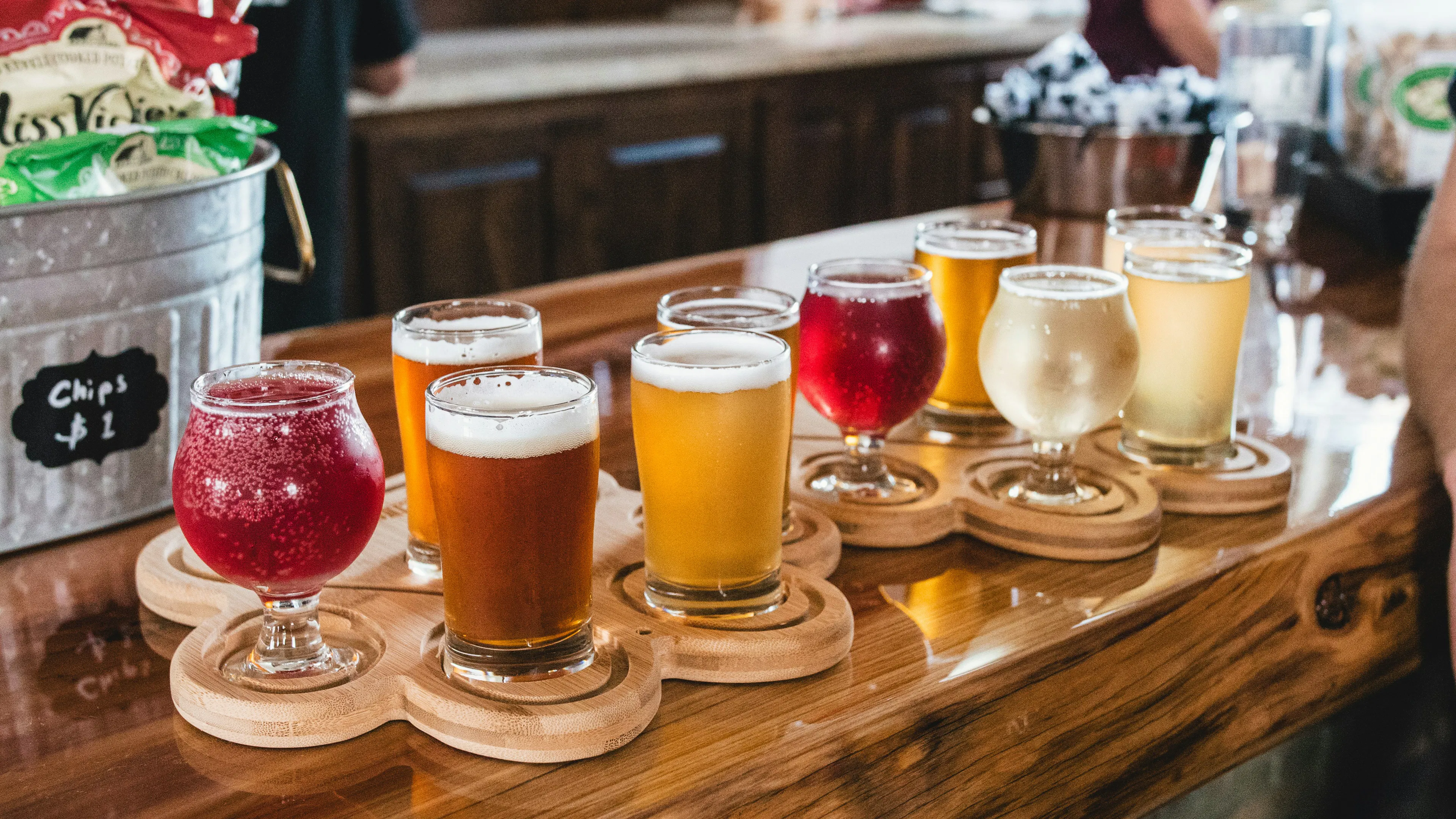 A wooden bar table with ten glassed of various ciders on a tasting tray