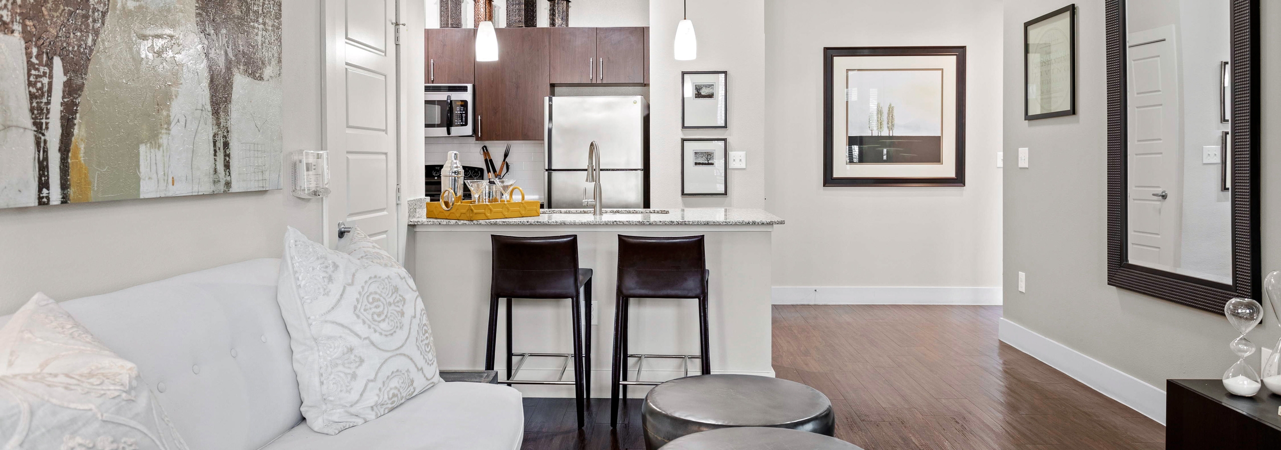 Apartment living room with whit couch and wood floor overlooking kitchen at AMLI at Escena apartments