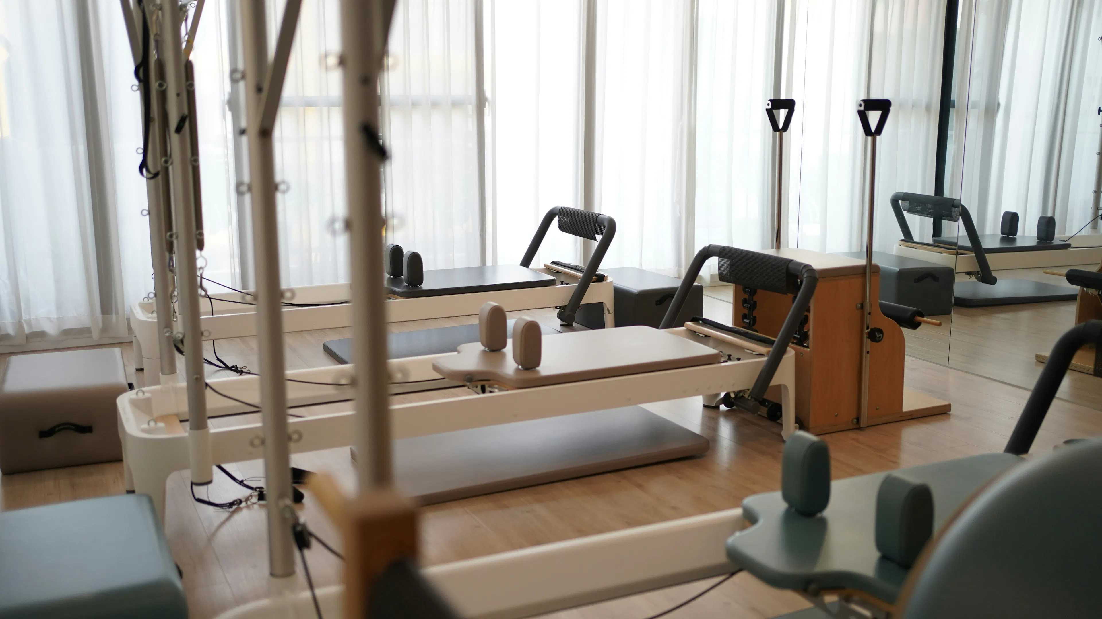 A row of Pilates exercise machines in a sunny studio room with a wall mirror