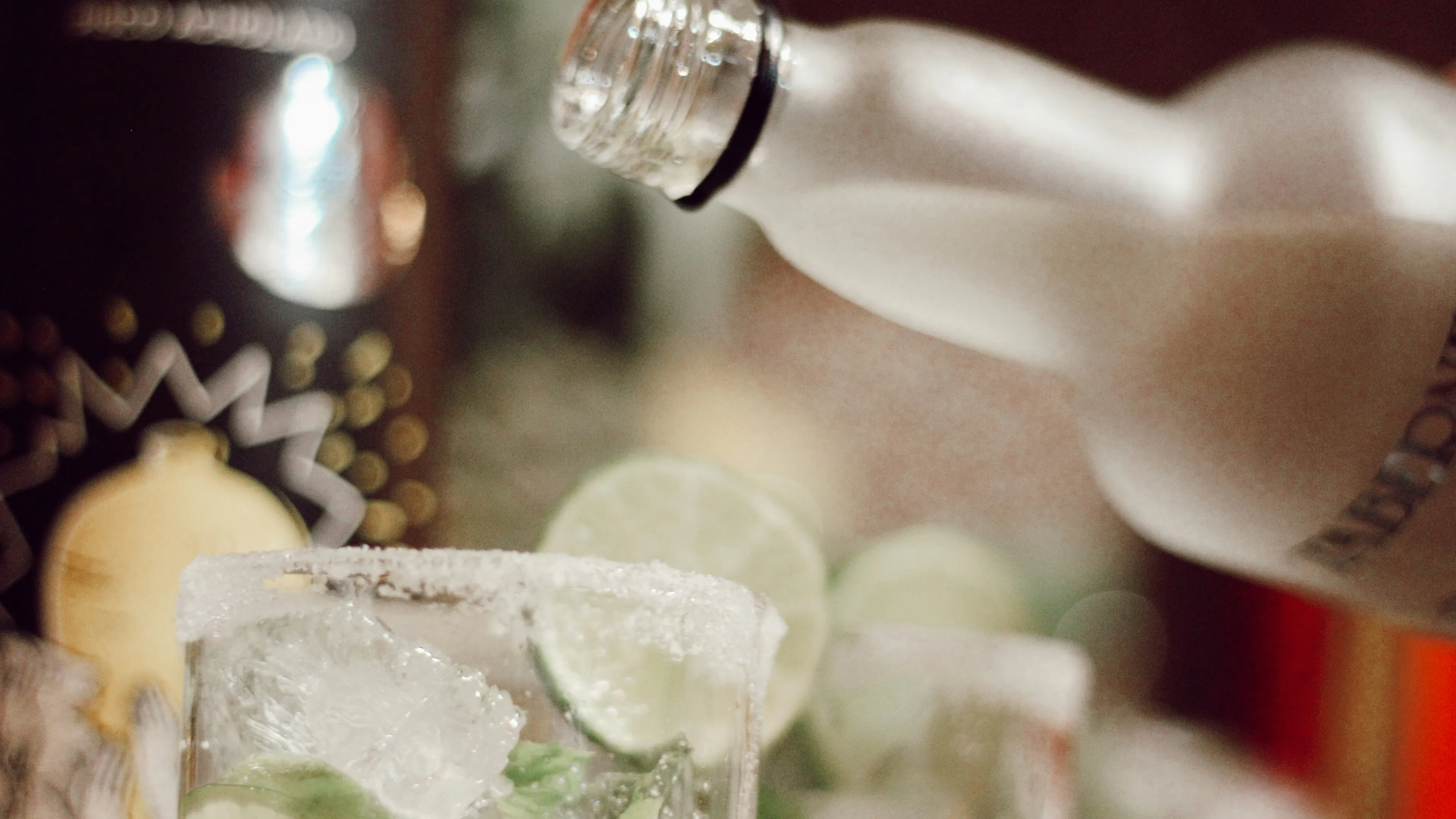A bottle of vodka being poured into a glass filled with ice and lime