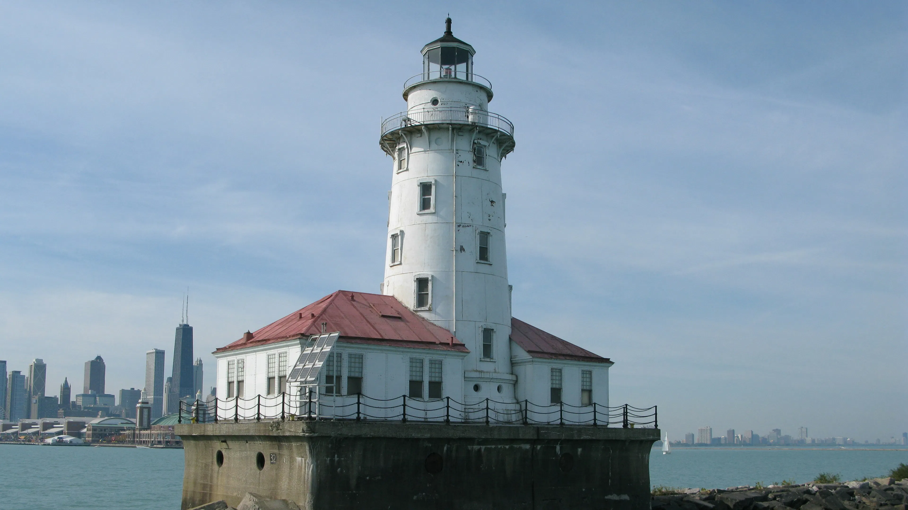 The red roof and white walls of the Chicago Harbor Lighthouse shining in the sunshine with the skyline of the city behind it