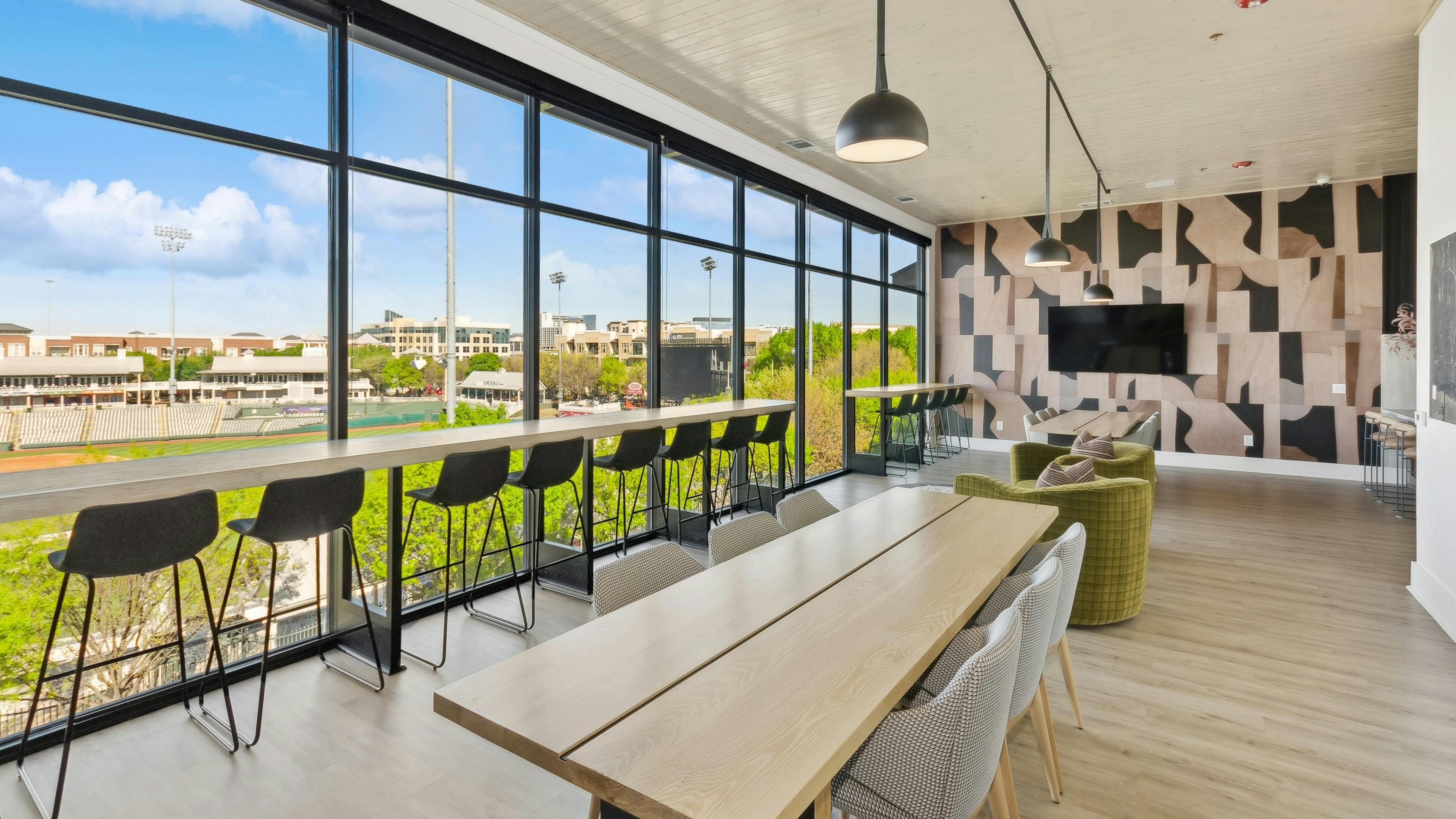 Sky lounge at AMLI at the Ballpark with a wall of windows featuring a long table ledge with high stools and long wood tables with chairs