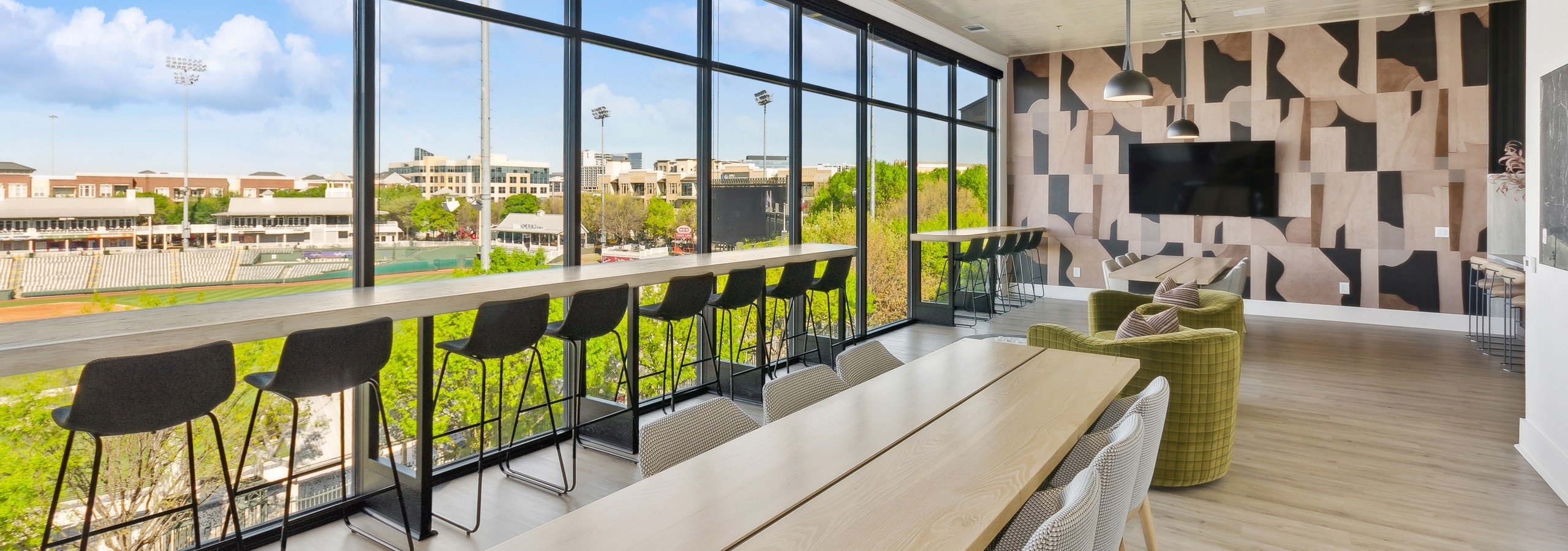 Sky lounge at AMLI at the Ballpark with a wall of windows featuring a long table ledge with high stools and long wood tables with chairs