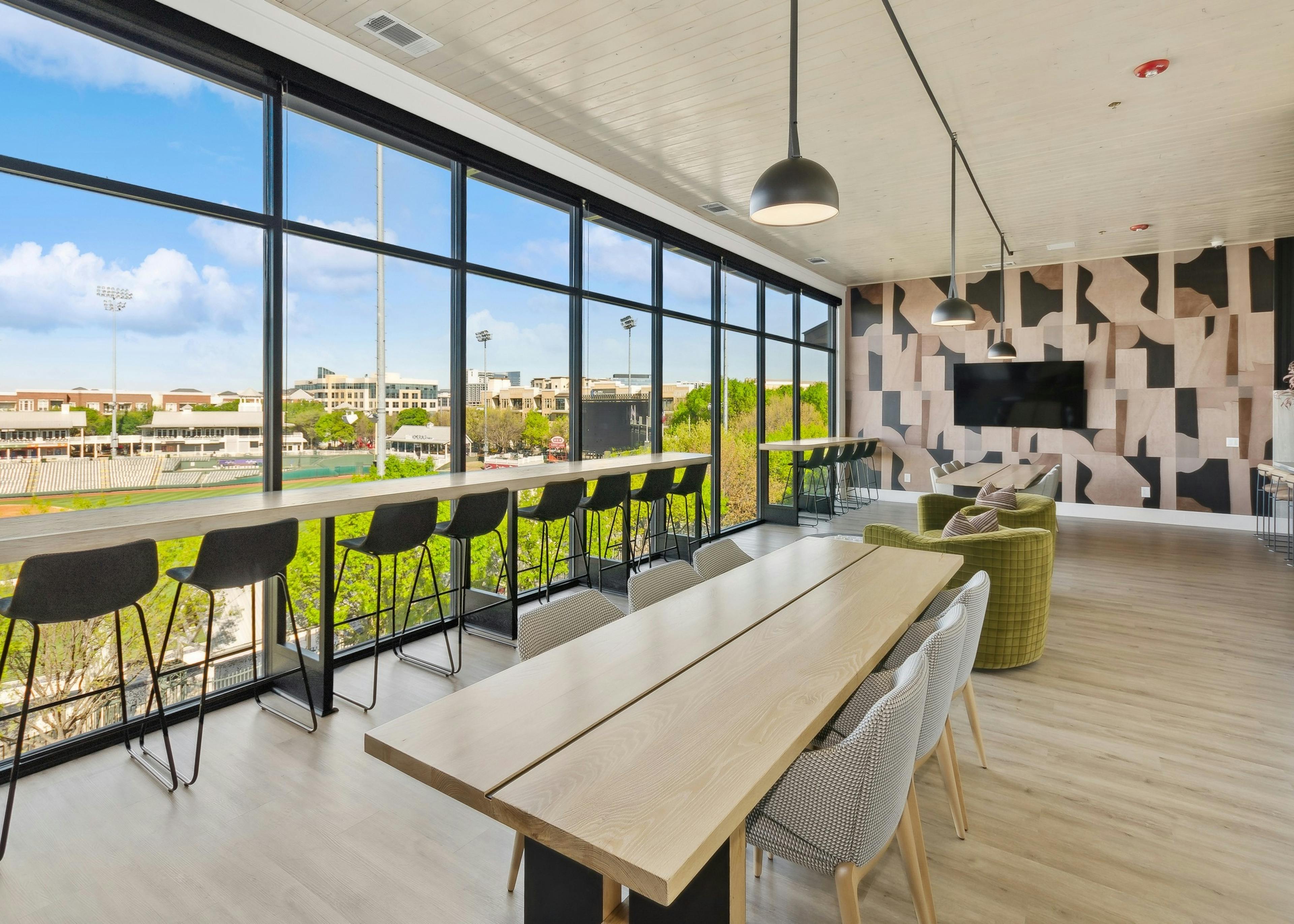 Sky lounge at AMLI at the Ballpark with a wall of windows featuring a long table ledge with high stools and long wood tables with chairs