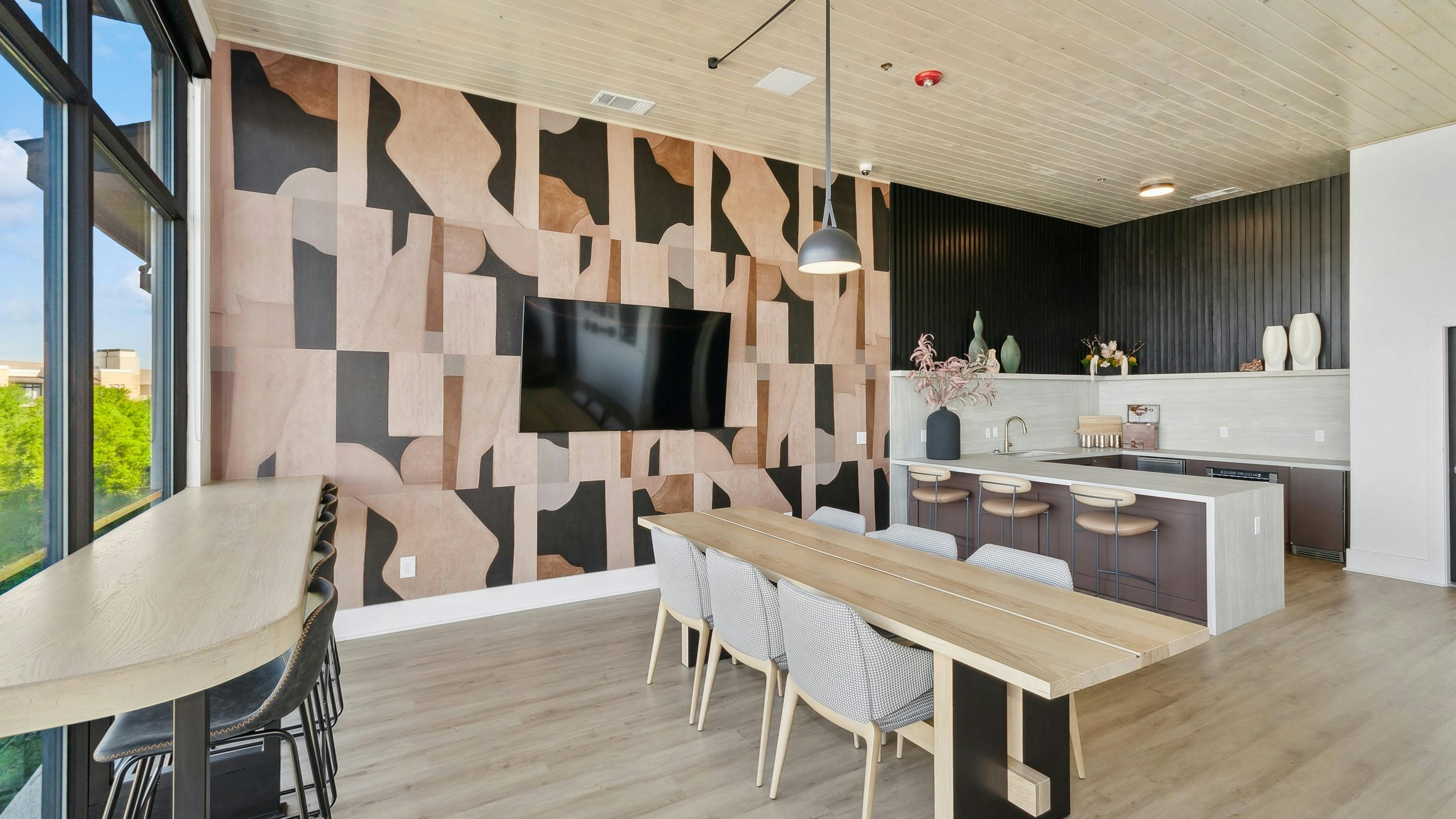 AMLI at the Ballpark sky lounge kitchen and dining area with wooden stables and geometric wall pattern with a mounted tv and hanging lights