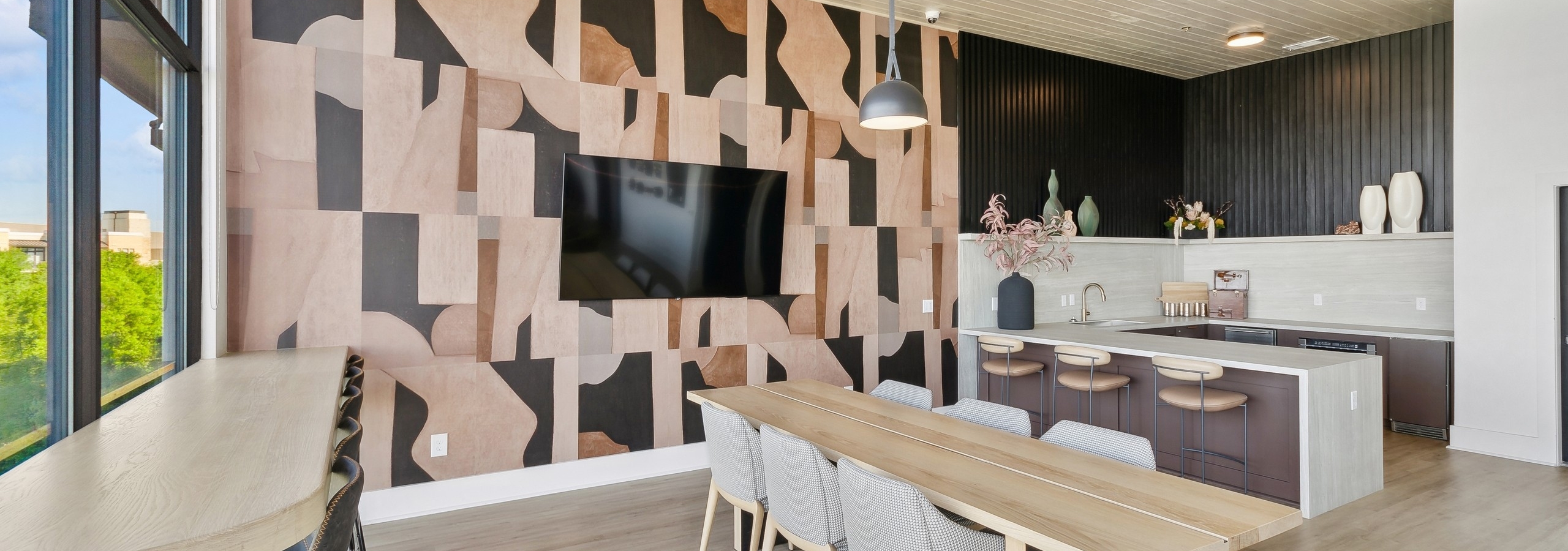 AMLI at the Ballpark sky lounge kitchen and dining area with wooden stables and geometric wall pattern with a mounted tv and hanging lights