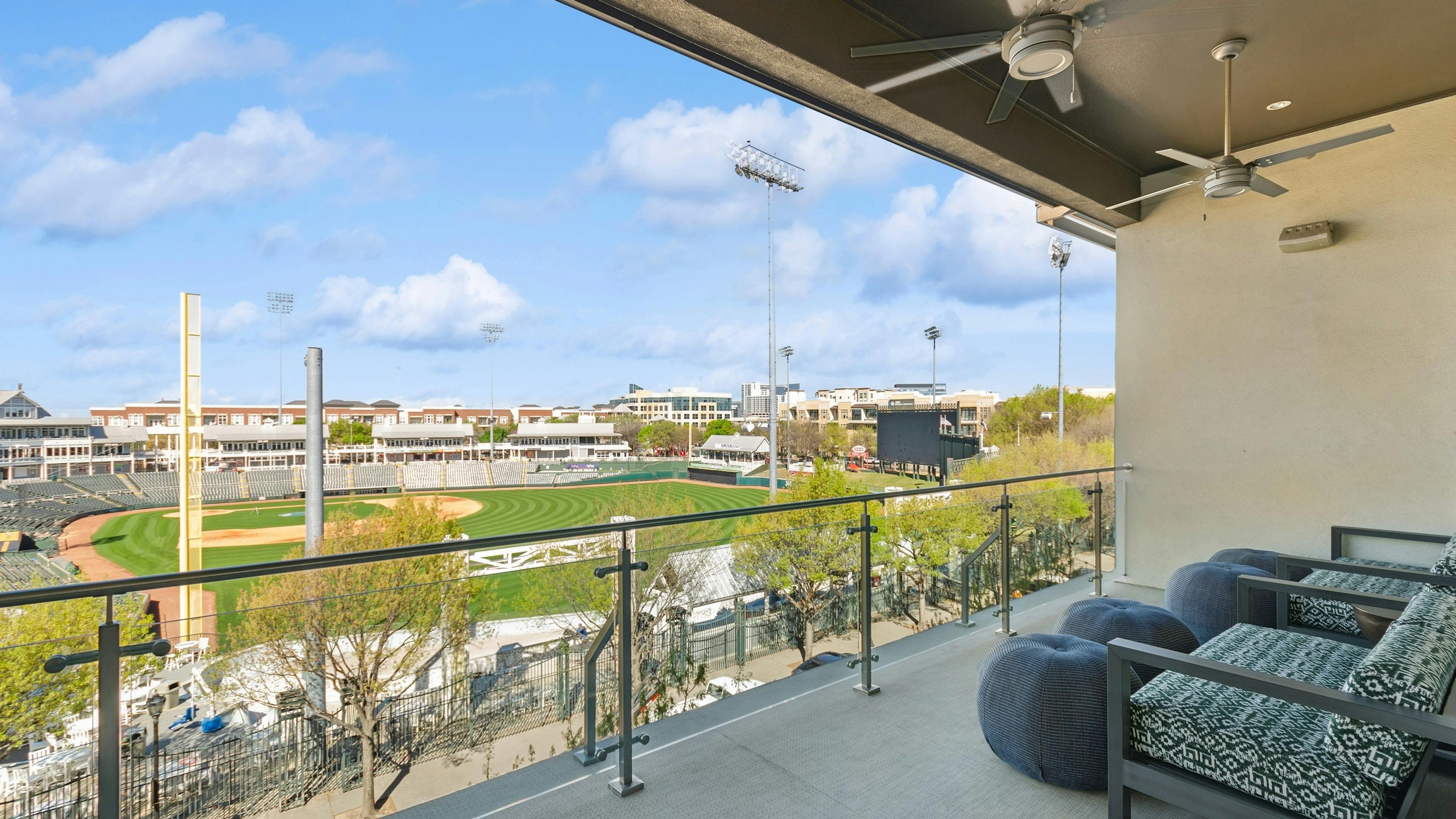 AMLI at the Ballpark large skybox balcony with two large chairs and four ottomans overlooking the ballpark under a clear blue sky
