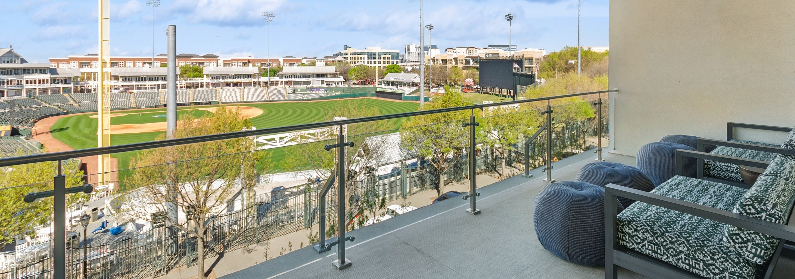AMLI at the Ballpark large skybox balcony with two large chairs and four ottomans overlooking the ballpark under a clear blue sky
