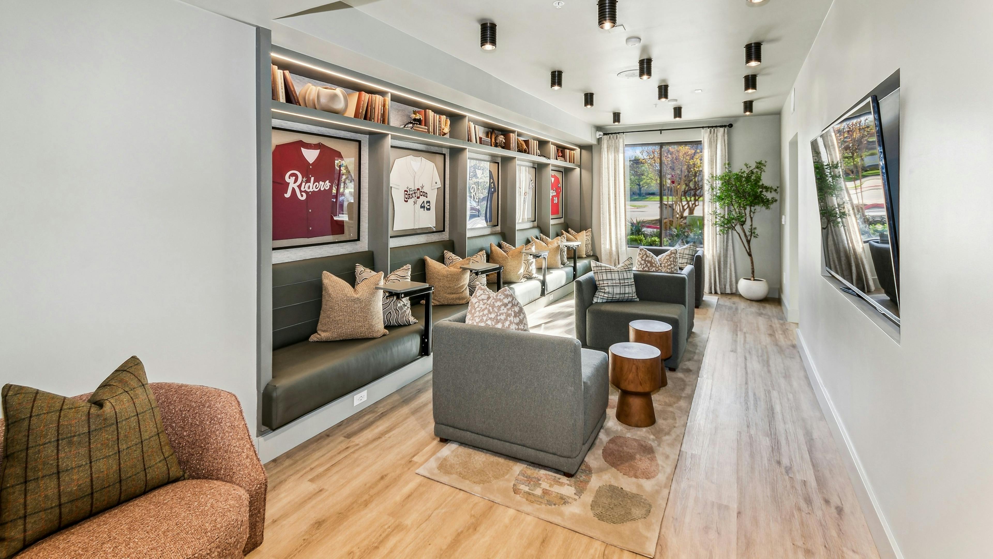 Media area in the co working lounge at AMLI at the Ballpark with 4 large chairs and bench seating with shelves with framed baseball jerseys 