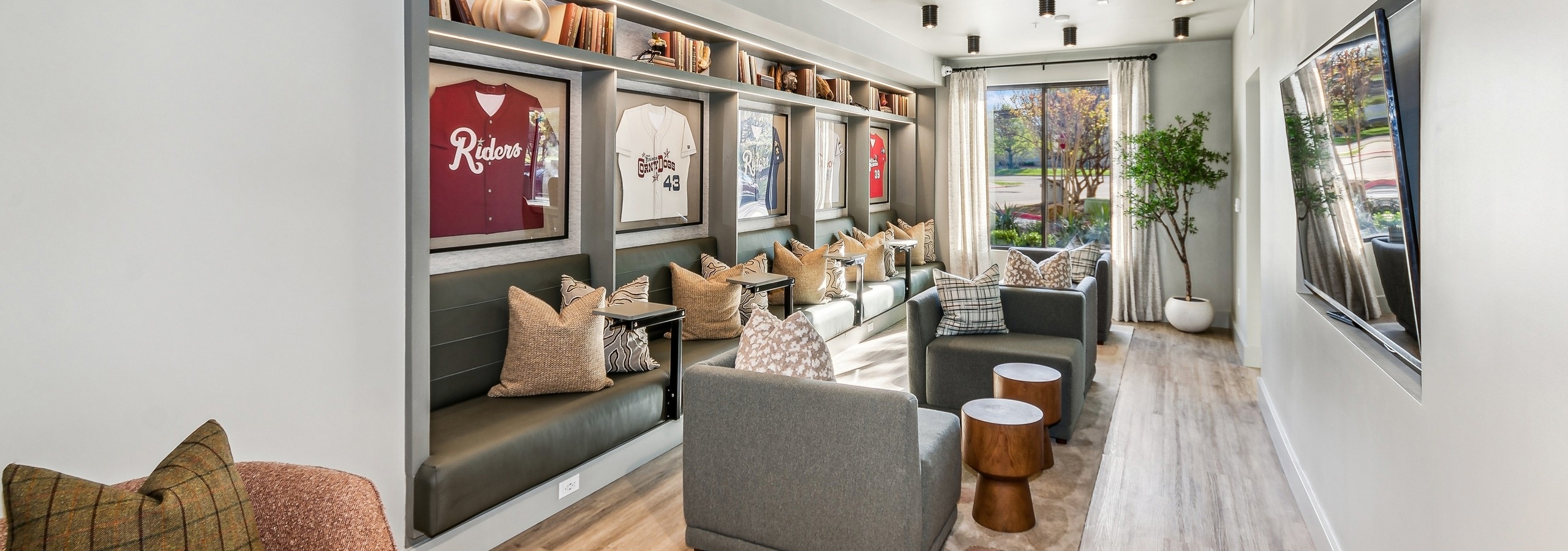 Media area in the co working lounge at AMLI at the Ballpark with 4 large chairs and bench seating with shelves with framed baseball jerseys