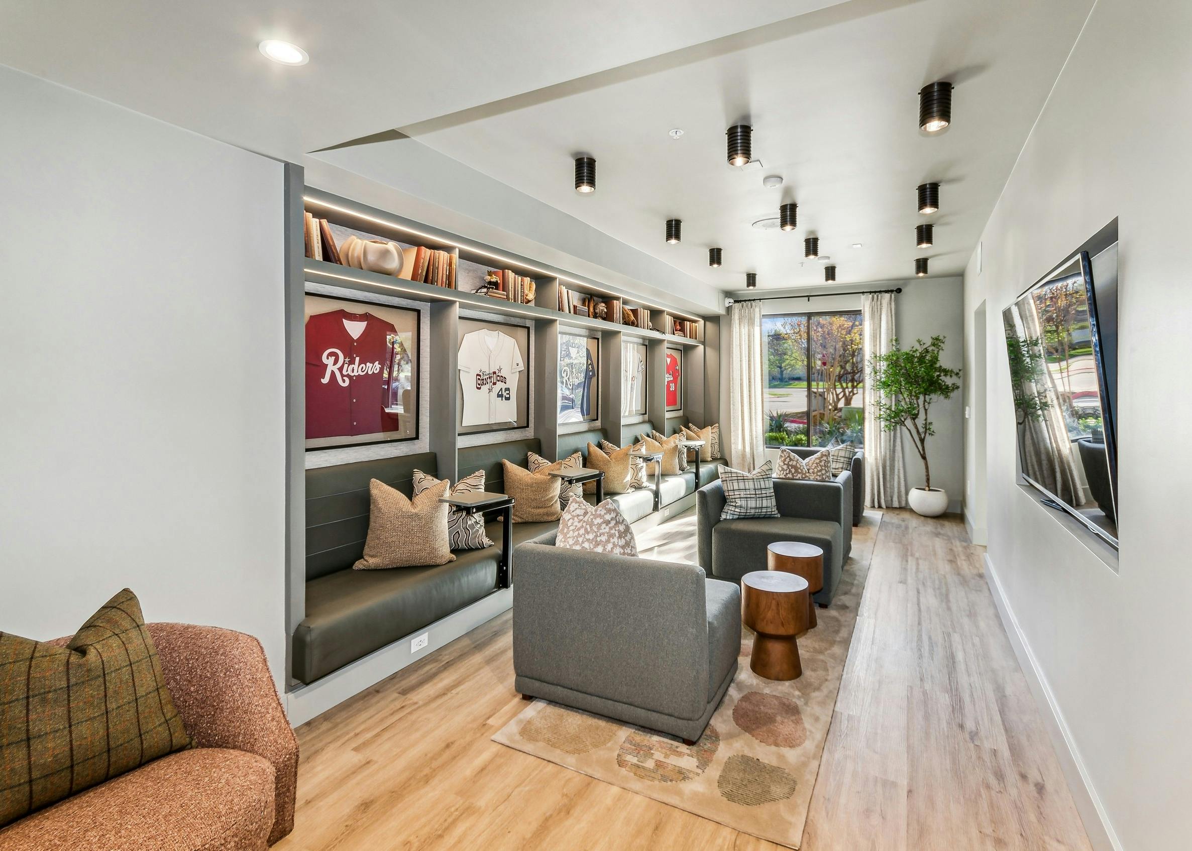 Media area in the co working lounge at AMLI at the Ballpark with 4 large chairs and bench seating with shelves with framed baseball jerseys