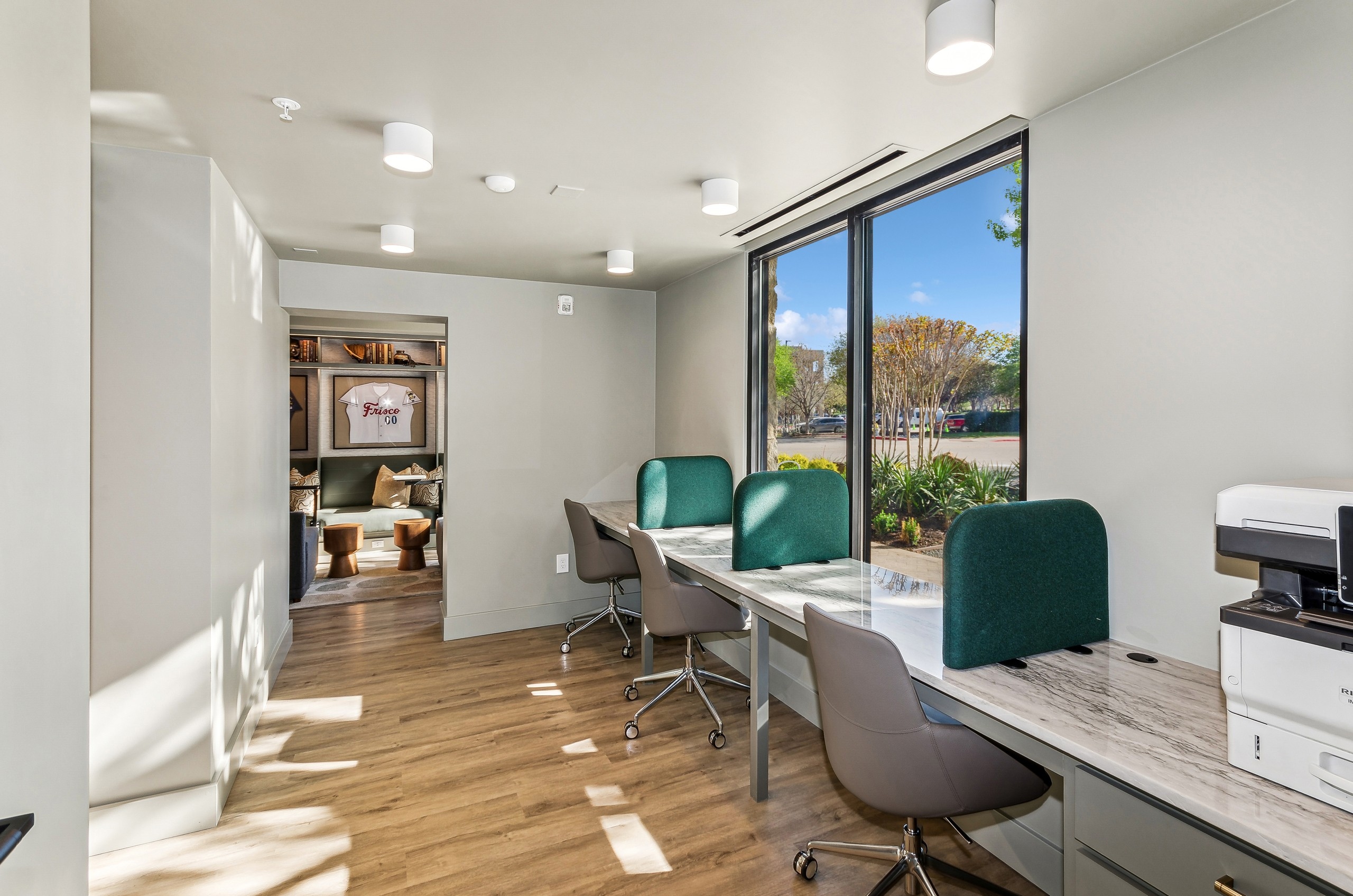 AMLI at the Ballpark business center featuring three work stations with rolling chairs with green padded dividers and a printer
