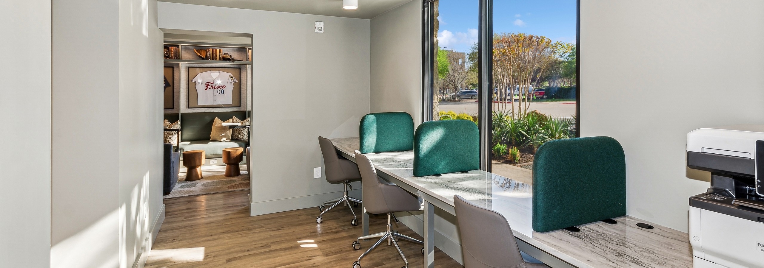 AMLI at the Ballpark business center featuring three work stations with rolling chairs with green padded dividers and a printer