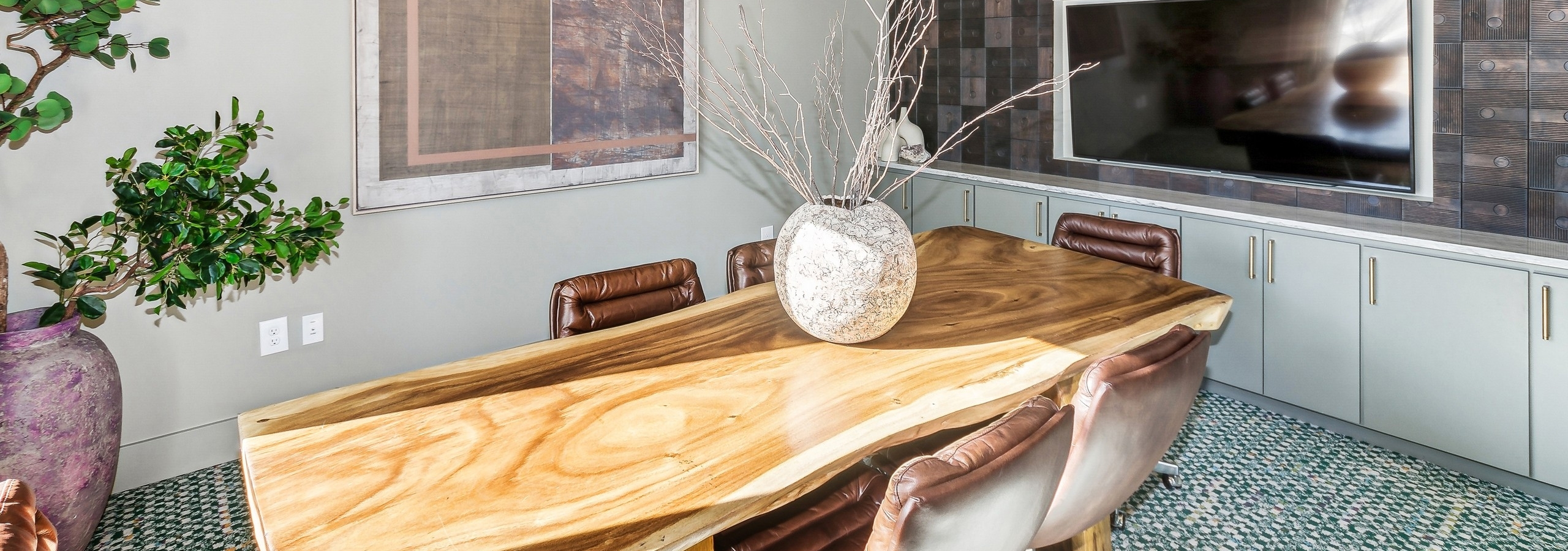 AMLI at the Ballpark conference room with a wooden table with a large vase surrounded by leather chairs and a wall with mounted tv