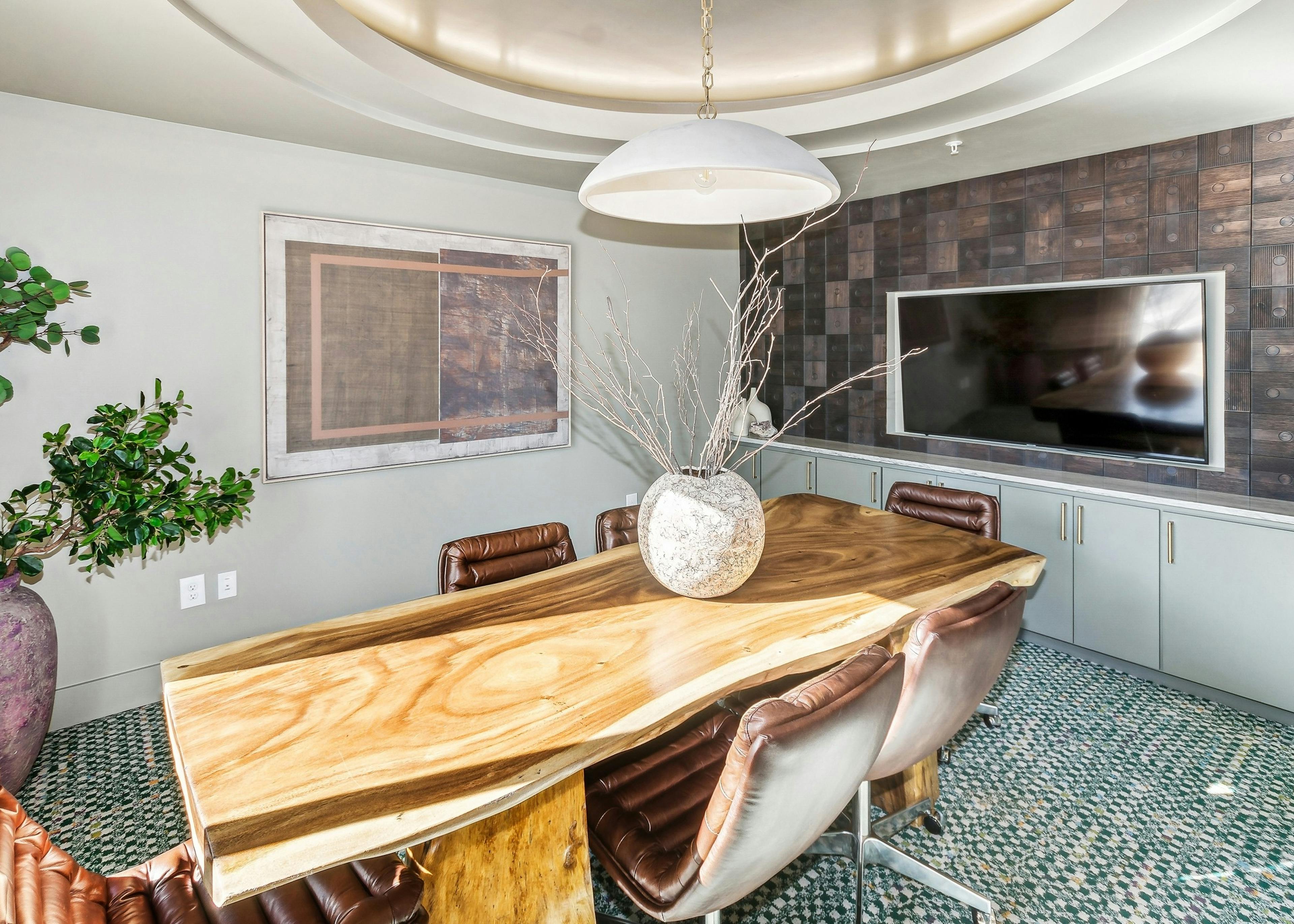 AMLI at the Ballpark conference room with a wooden table with a large vase surrounded by leather chairs and a wall with mounted tv 