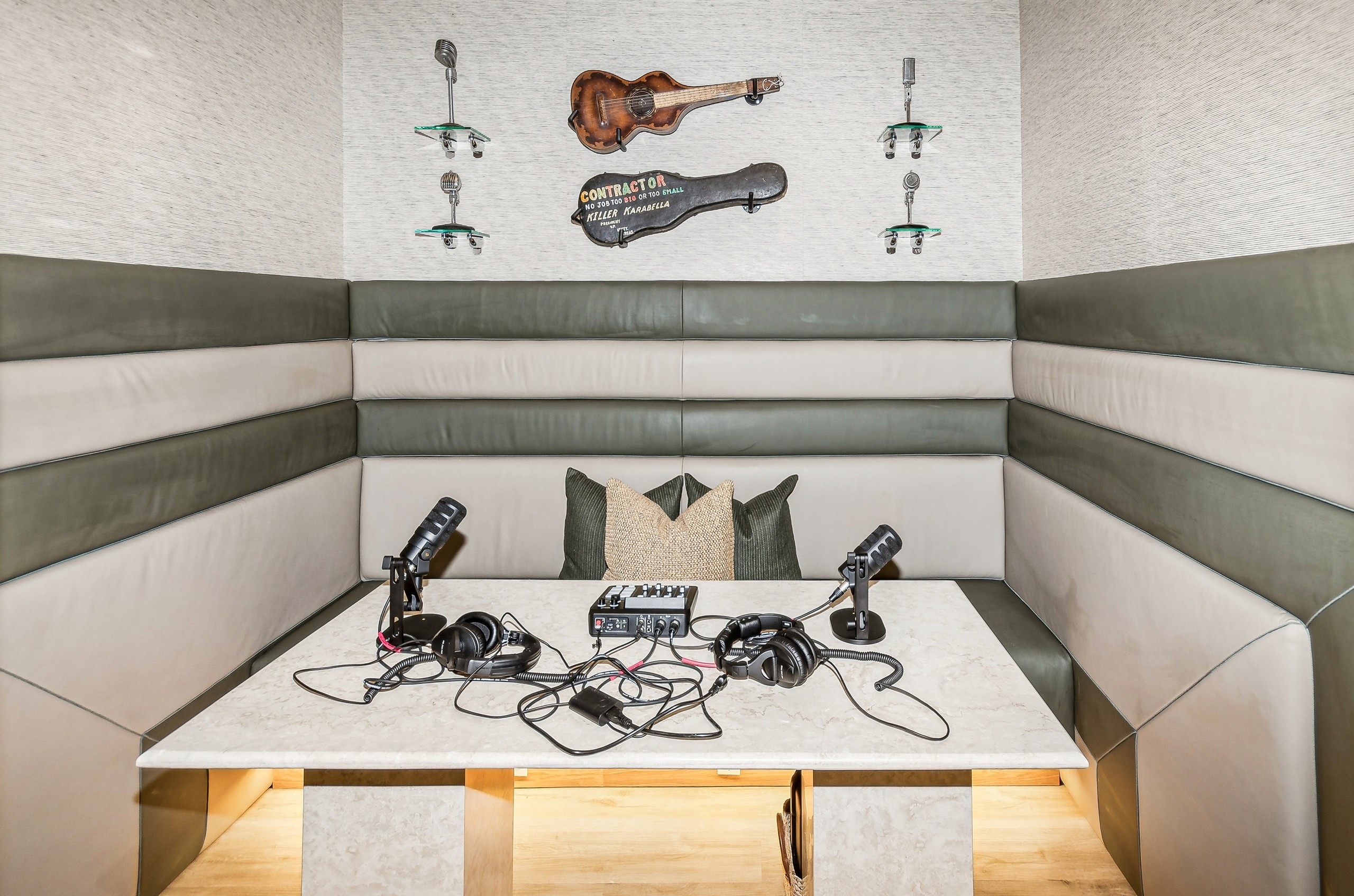 Podcast room with booth seating and olive and beige padded walls surrounding quartz table with recording equipment at AMLI at the Ballpark