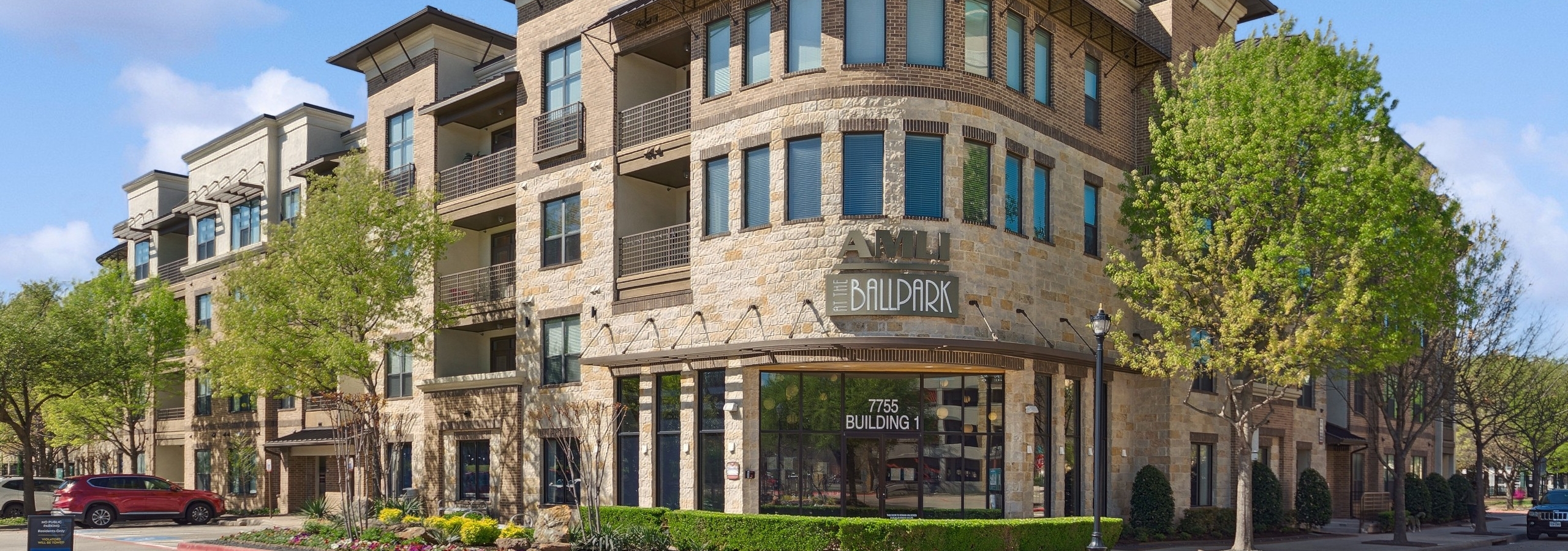 View of the beige brick exterior of AMLI at the Ballpark leasing office entry with the property logo on a sunny day with clear blue skies.