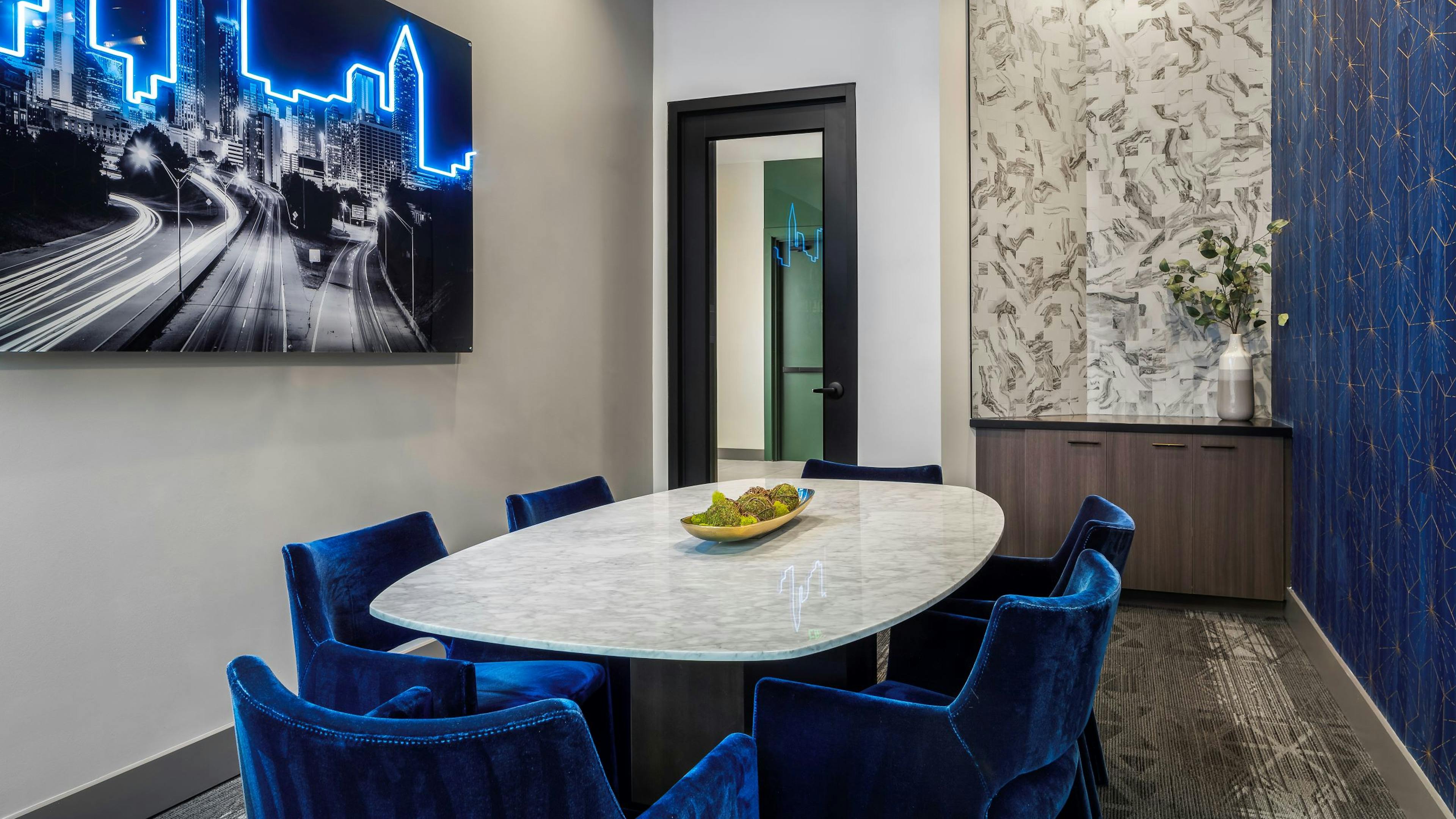 AMLI Flatiron conference room with white table and 6 blue velvet chairs and wood tone cabinet with black and blue neon artwork