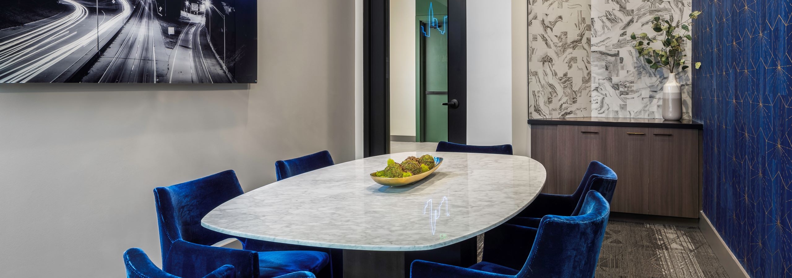 AMLI Flatiron conference room with white table and 6 blue velvet chairs and wood tone cabinet with black and blue neon artwork