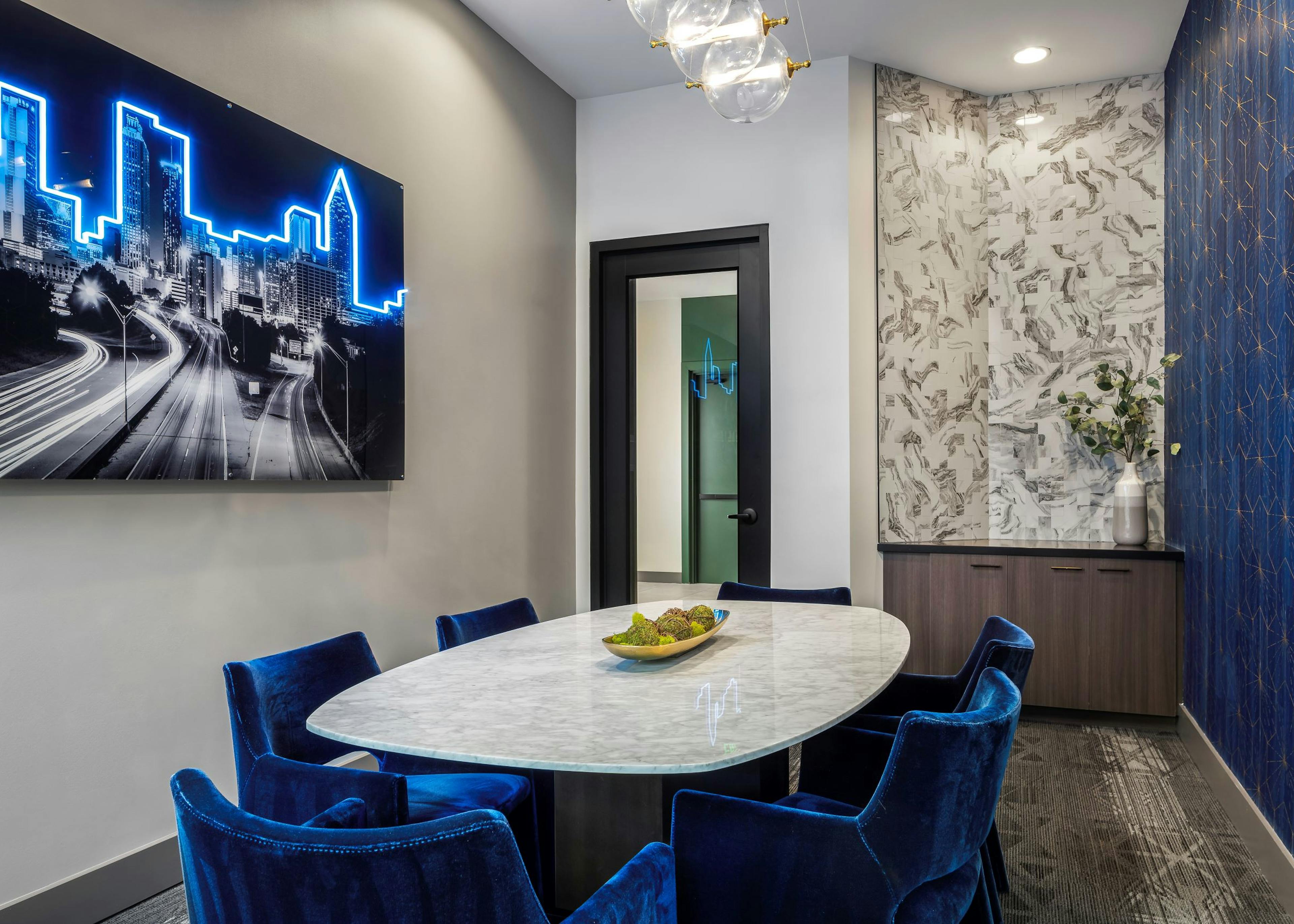 AMLI Flatiron conference room with white table and 6 blue velvet chairs and wood tone cabinet with black and blue neon artwork