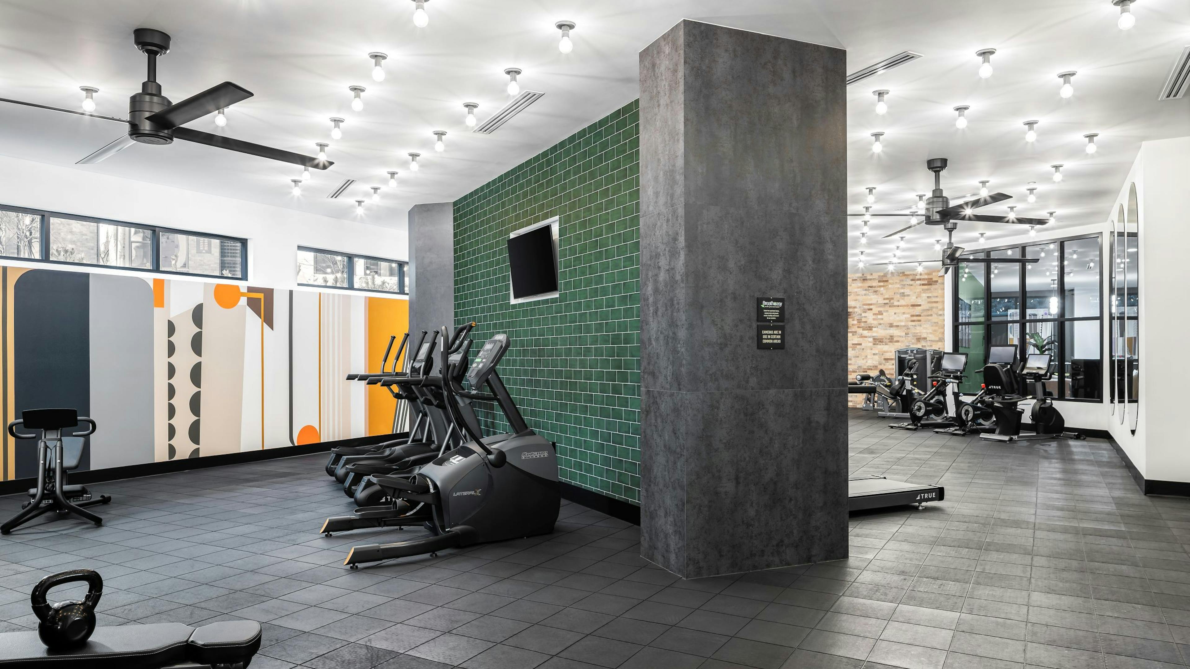 AMLI Flatiron fitness center with racks of weights and two benches and cardio equipment in front of green tile wall