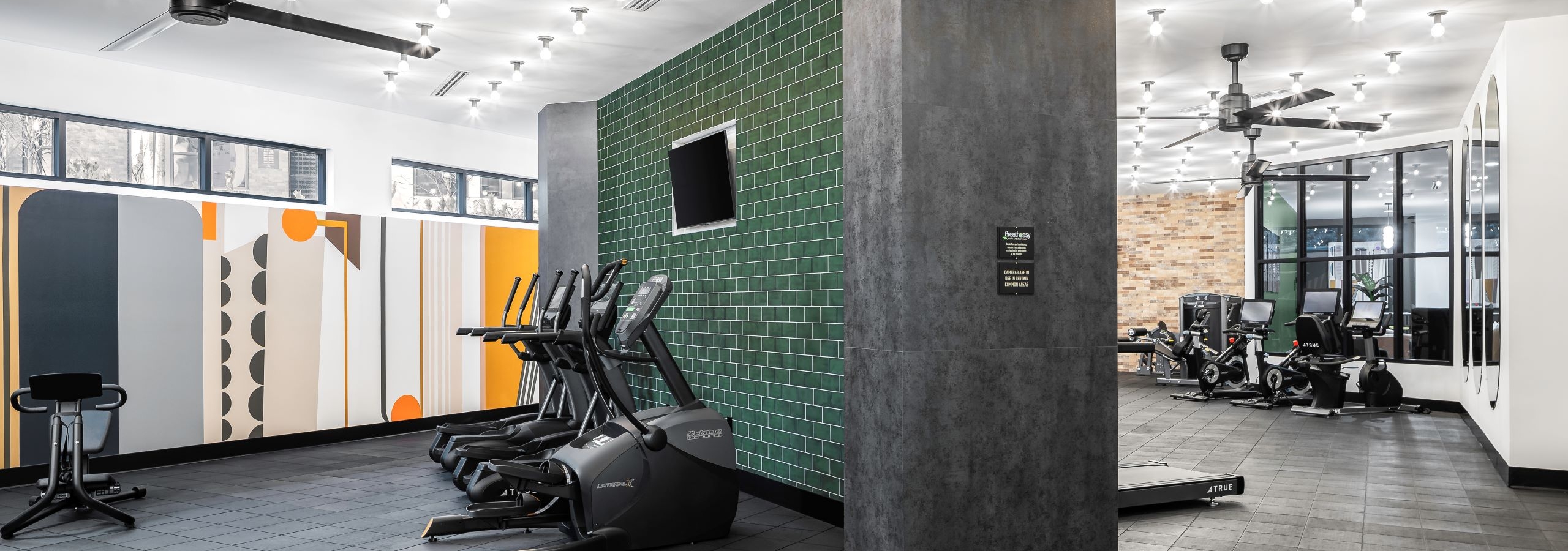 AMLI Flatiron fitness center with racks of weights and two benches and cardio equipment in front of green tile wall