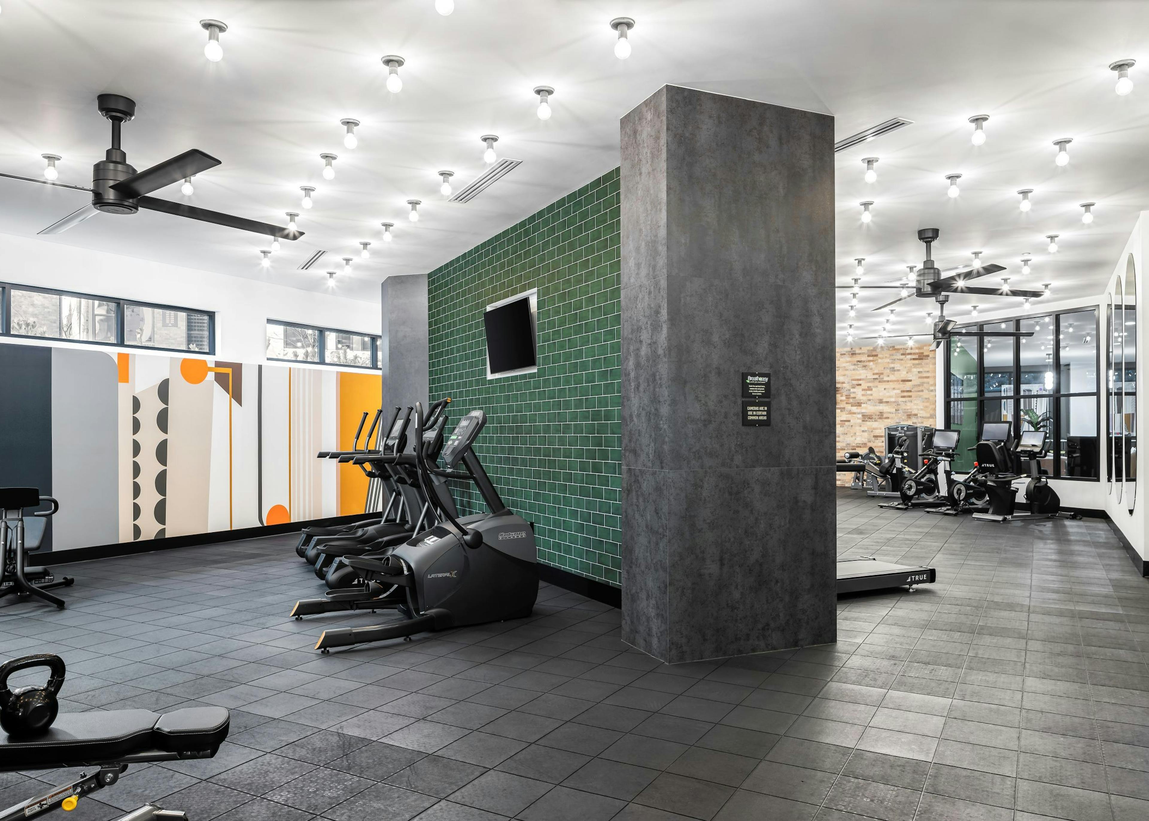 AMLI Flatiron fitness center with racks of weights and two benches and cardio equipment in front of green tile wall