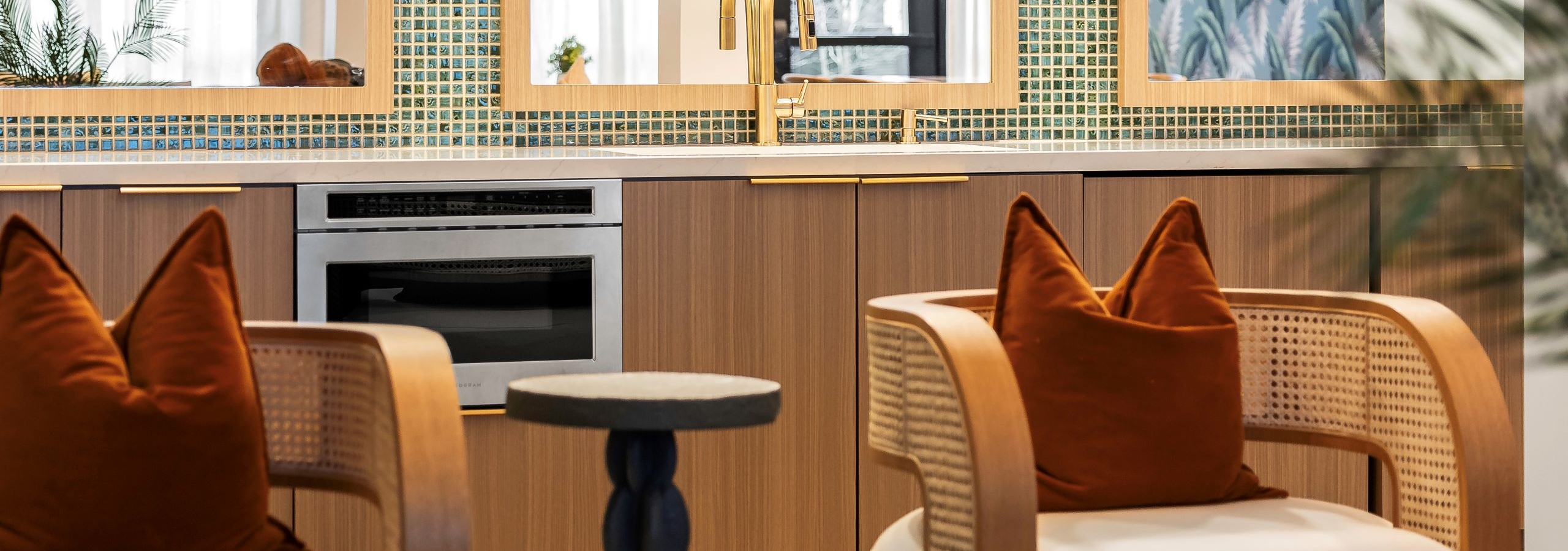 AMLI Flatiron pool clubroom with two beige chairs with white cushions and orange pillows and a small black side table in front of a kitchen counter