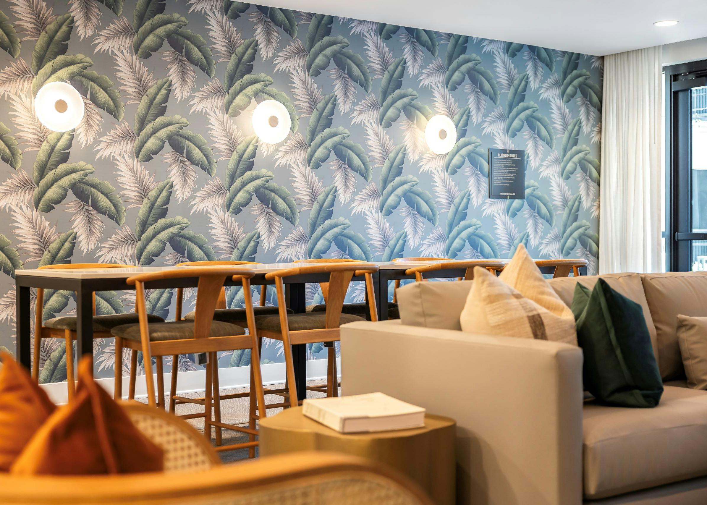 Pool club at AMLI Flatiron with 8 wood stools surrounding a long bar height table set against blue and green wallpaper with a leaf design