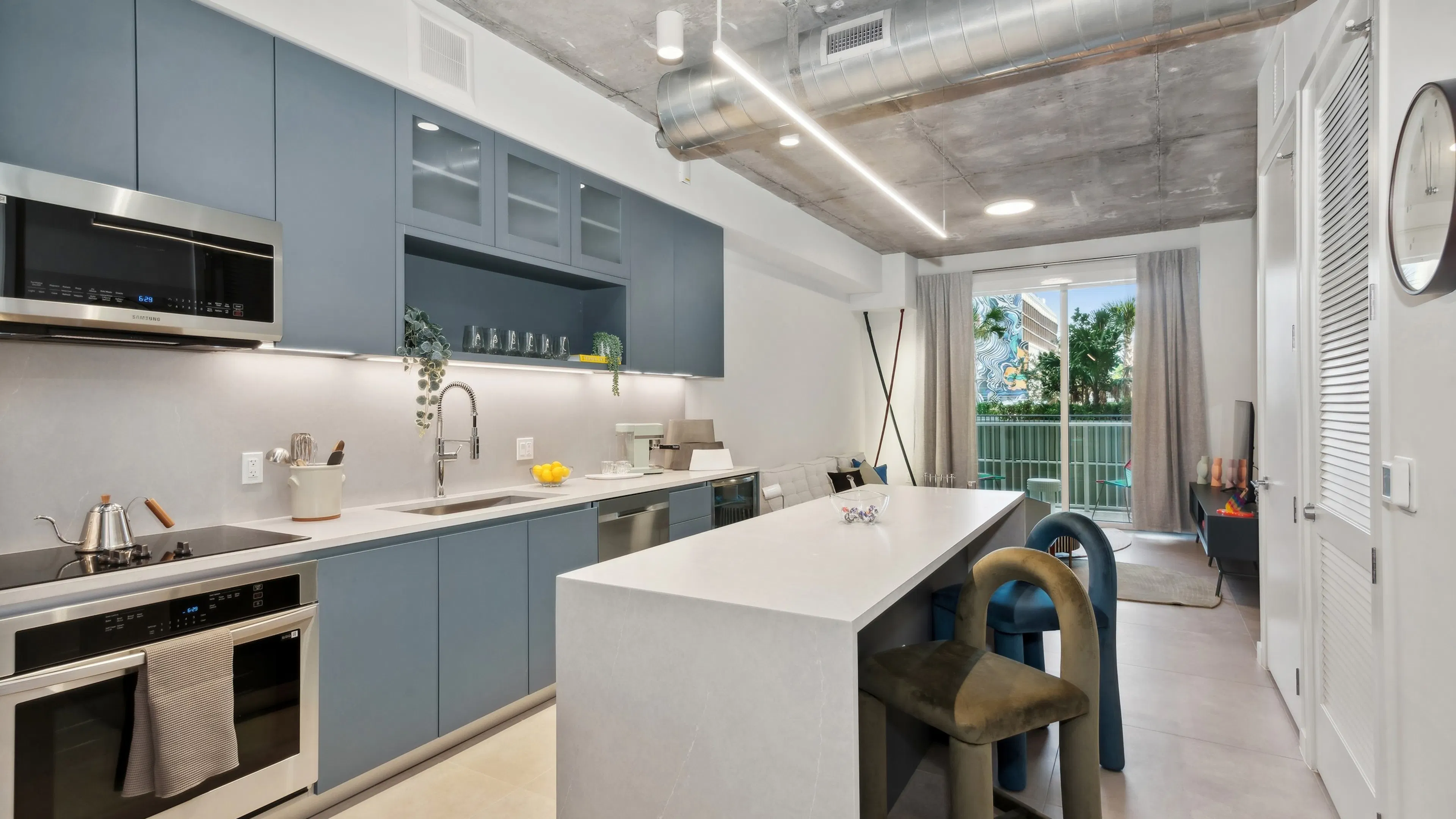 Modern AMLI Wynwood kitchen with blue cabinets and stainless steel appliances and a white island extending to the living area with a view to patio