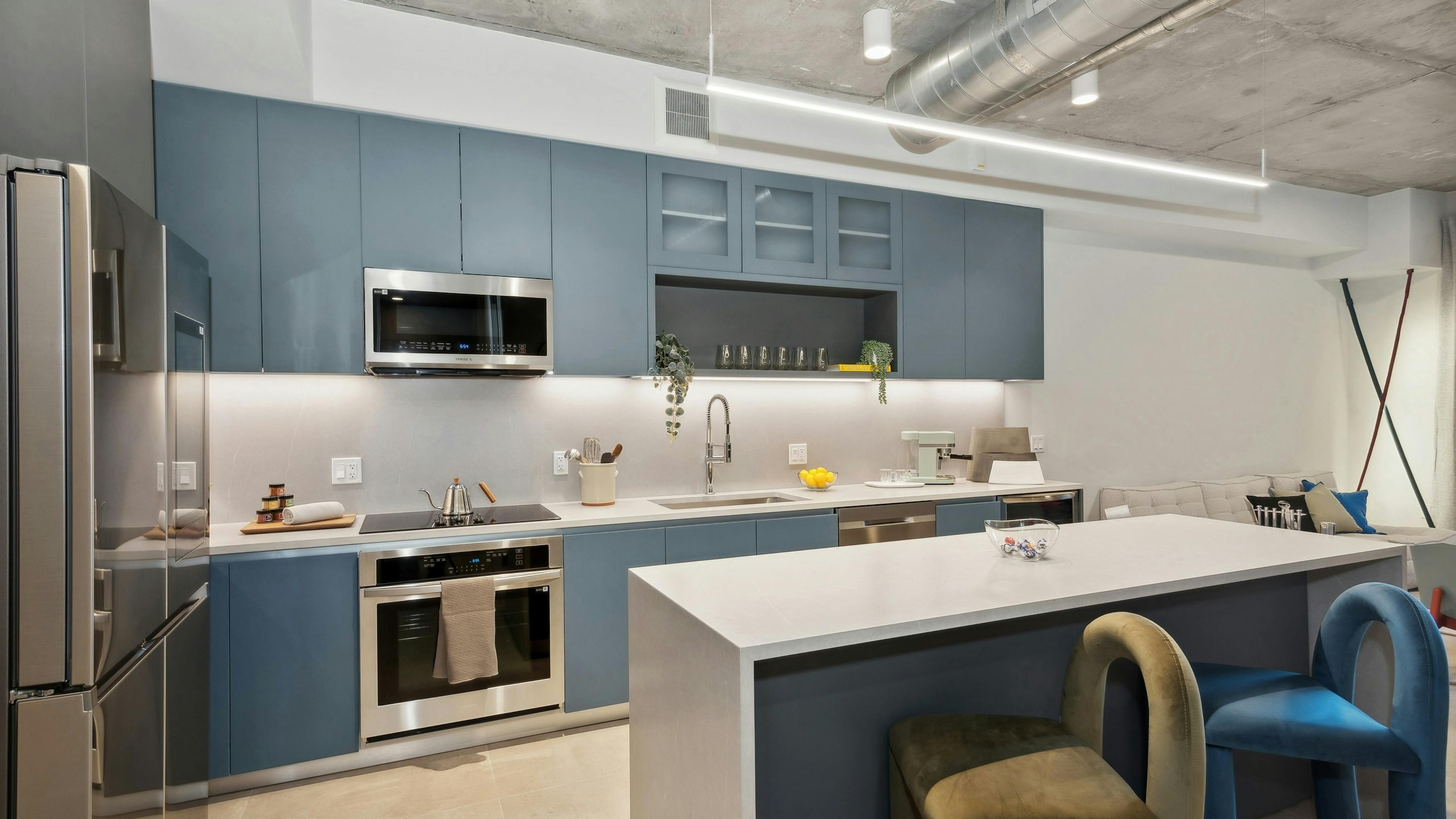 Modern kitchen at AMLI Wynwood apartments with sleek blue cabinetry and stainless steel appliances and a white quartz island with 2 colorful stools