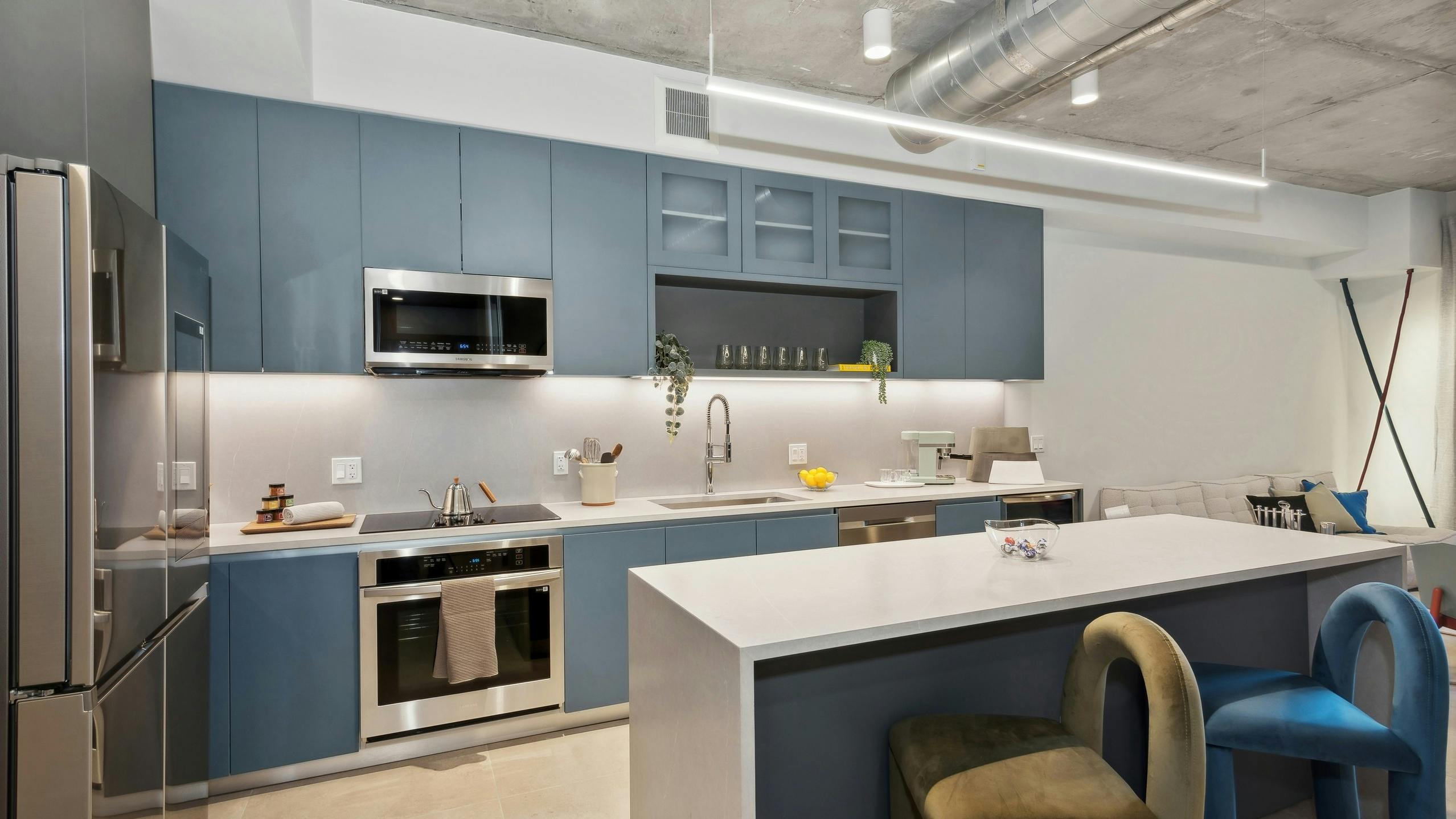 Modern kitchen at AMLI Wynwood apartments with sleek blue cabinetry and stainless steel appliances and a white quartz island with 2 colorful stools