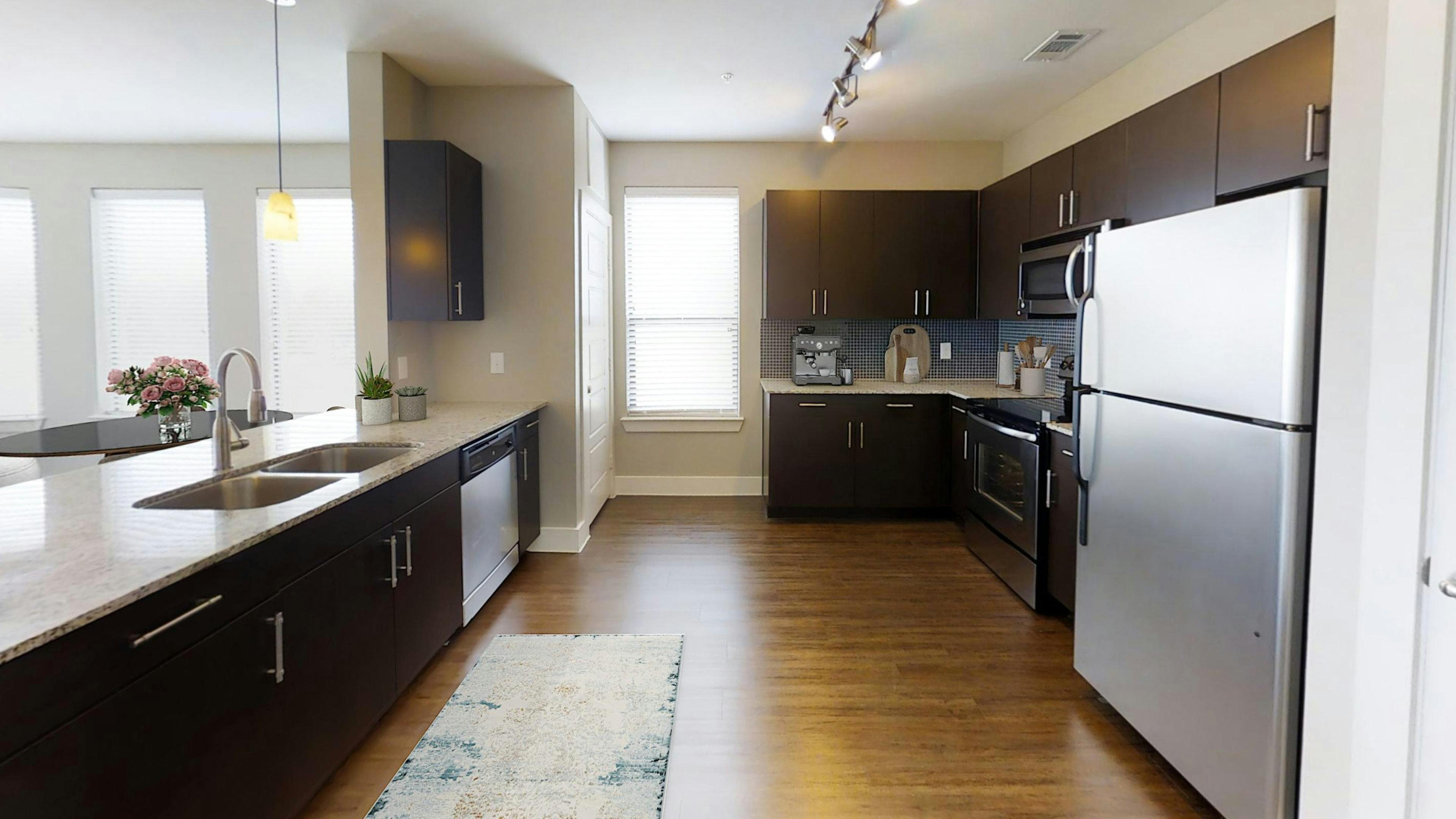 AMLI at the Ballpark kitchen featuring dark brown cabinetry and light granite countertops and stainless-steel appliances with hardwood floors