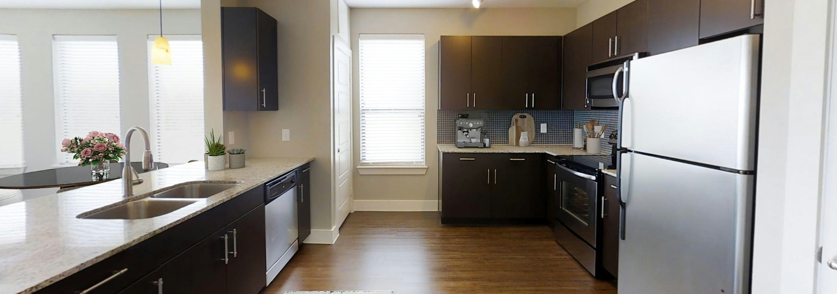 AMLI at the Ballpark kitchen featuring dark brown cabinetry and light granite countertops and stainless-steel appliances with hardwood floors