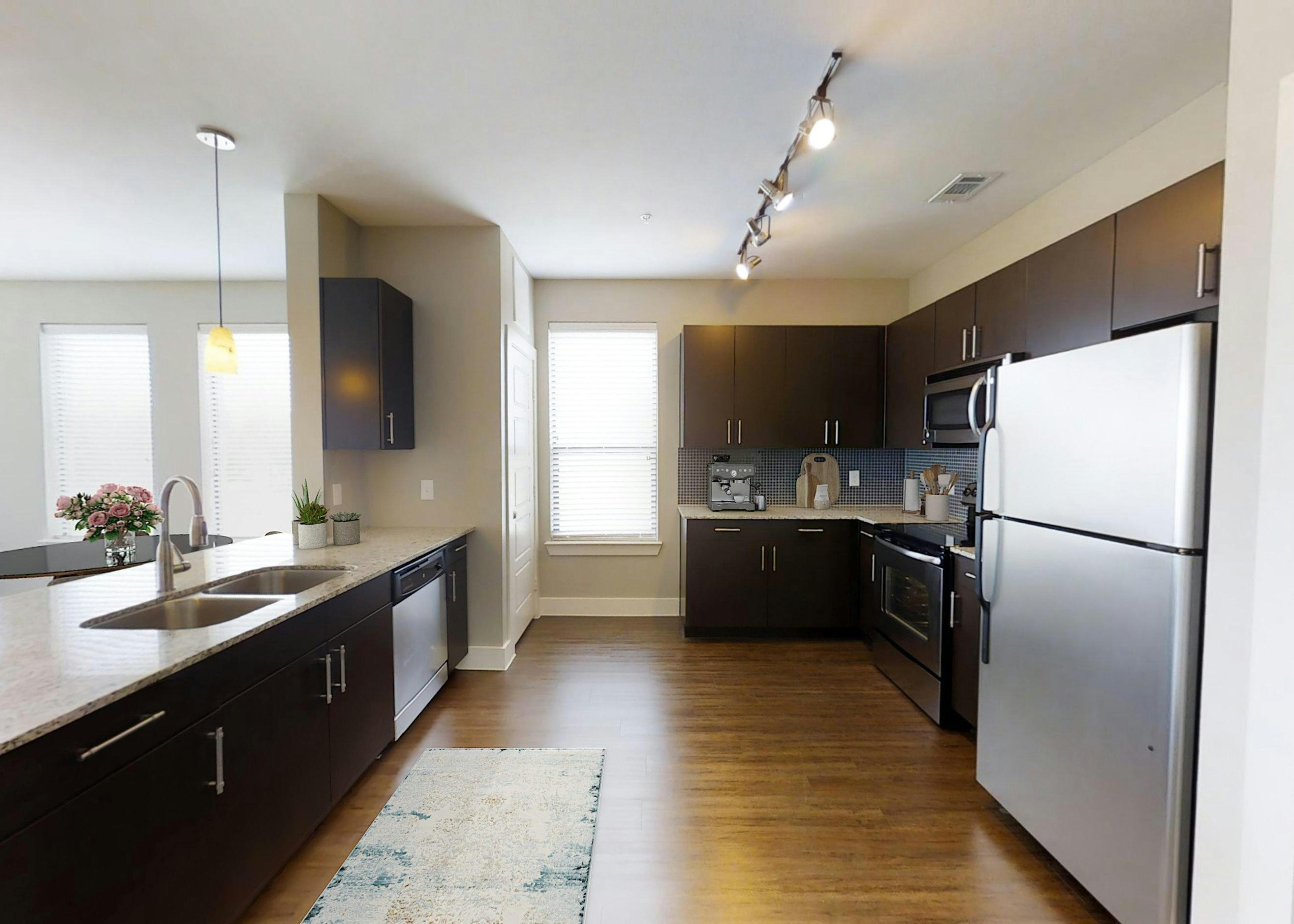 AMLI at the Ballpark kitchen featuring dark brown cabinetry and light granite countertops and stainless-steel appliances with hardwood floors