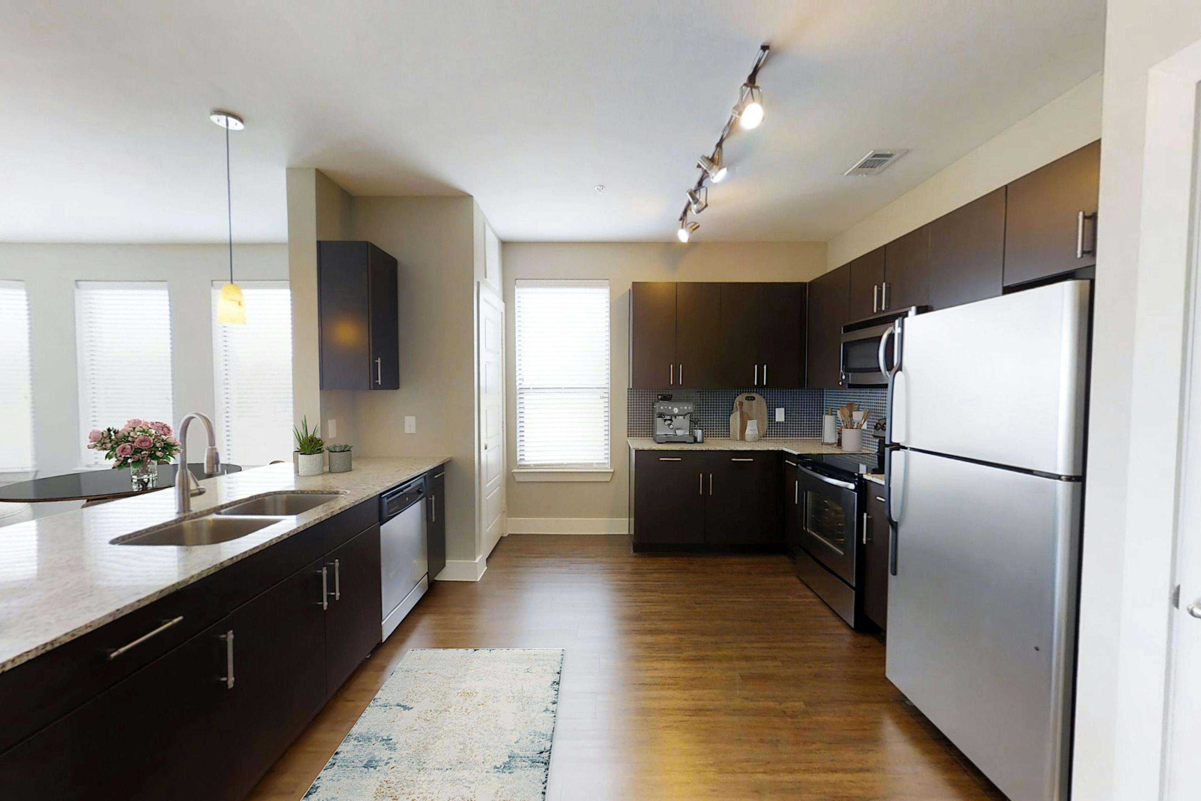 AMLI at the Ballpark kitchen featuring dark brown cabinetry and light granite countertops and stainless-steel appliances with hardwood floors