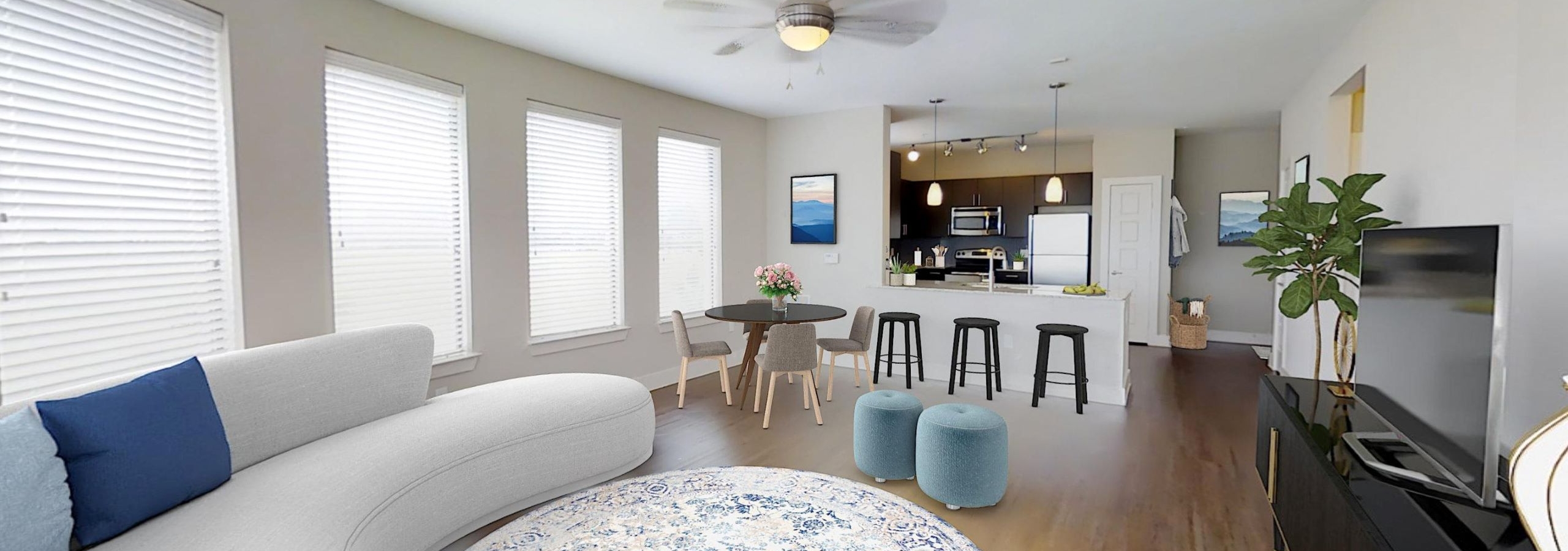 An apartment living room with a white couch and round light rug with a TV and dining area and view into the kitchen at AMLI at the Ballpark