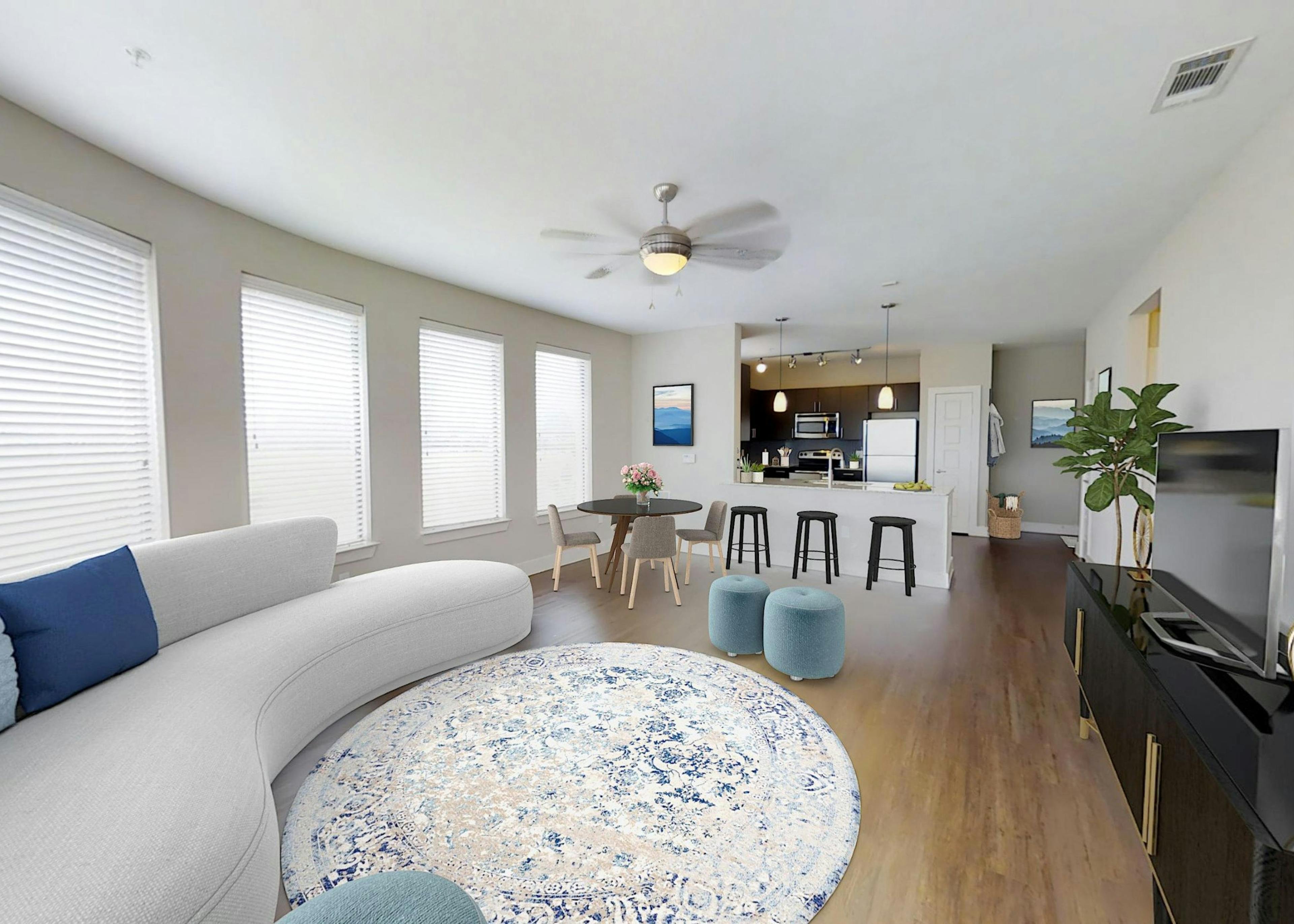 An apartment living room with a white couch and round light rug with a TV and dining area and view into the kitchen at AMLI at the Ballpark