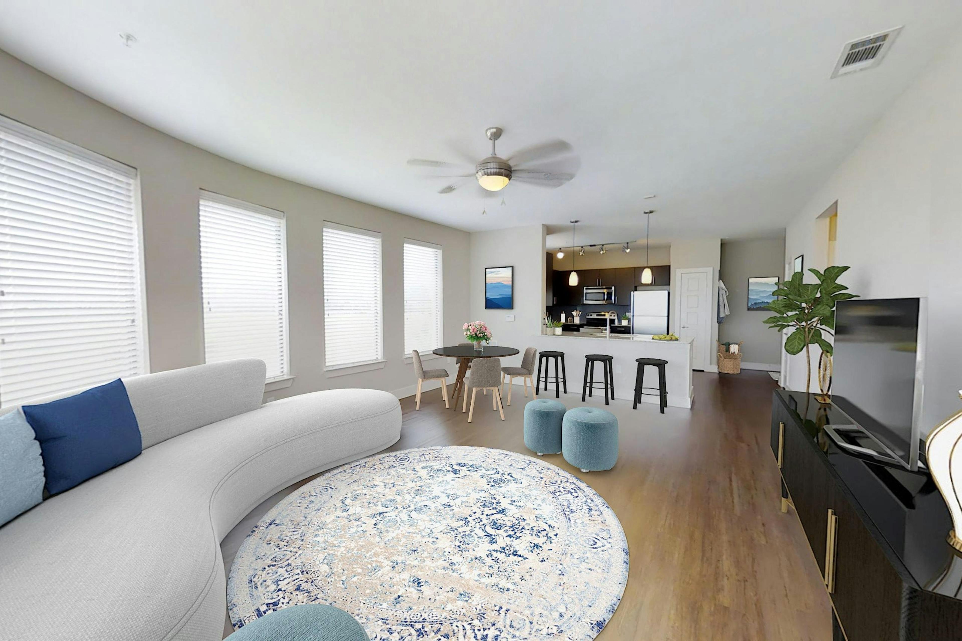 An apartment living room with a white couch and round light rug with a TV and dining area and view into the kitchen at AMLI at the Ballpark