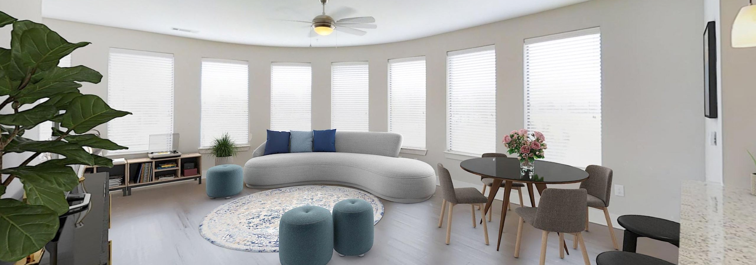 Living room at AMLI at the Ballpark featuring a wall of windows above a curved white sofa and a dining area with a wood table set