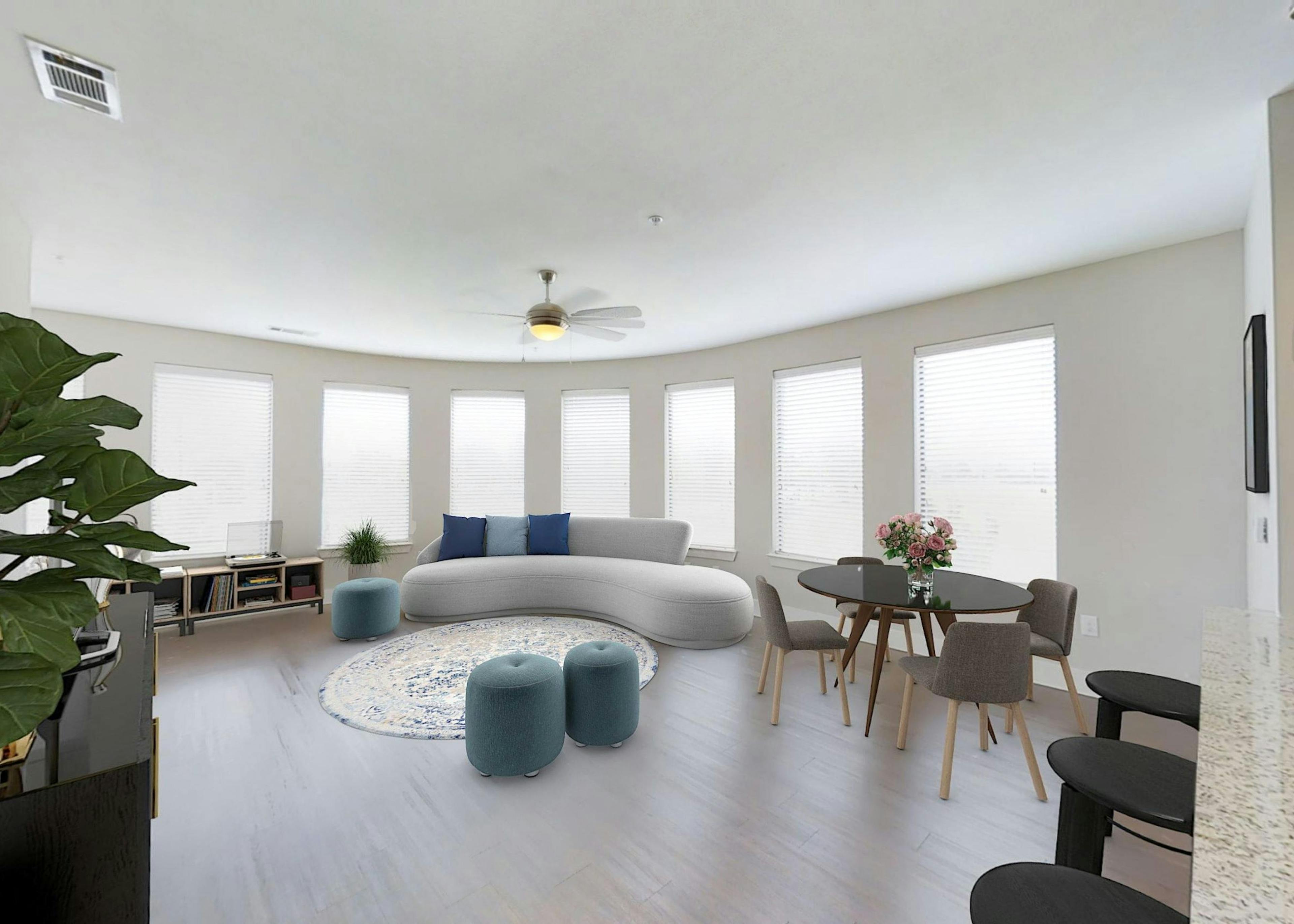 Living room at AMLI at the Ballpark featuring a wall of windows above a curved white sofa and a dining area with a wood table set