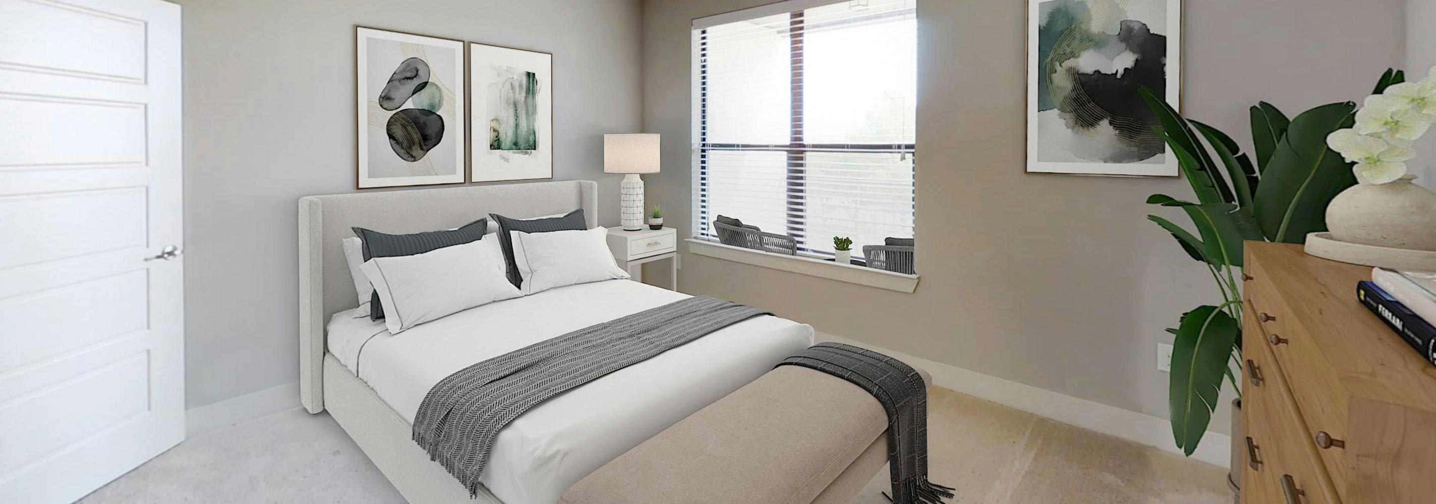 AMLI at the Ballpark bedroom featuring a bed with gray and white linens and a bench at the foot and a nearby window and art on the walls