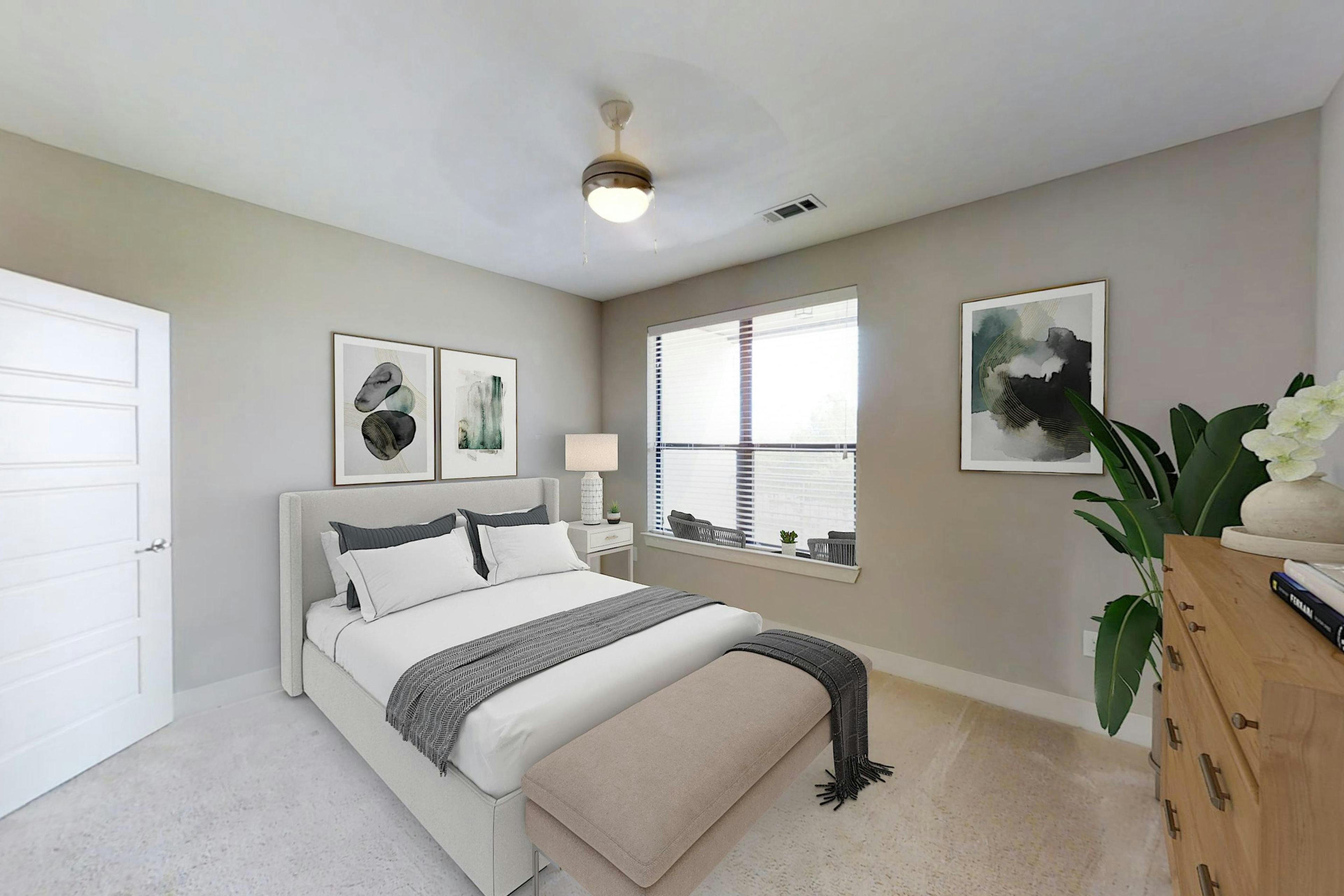 AMLI at the Ballpark bedroom featuring a bed with gray and white linens and a bench at the foot and a nearby window and art on the walls